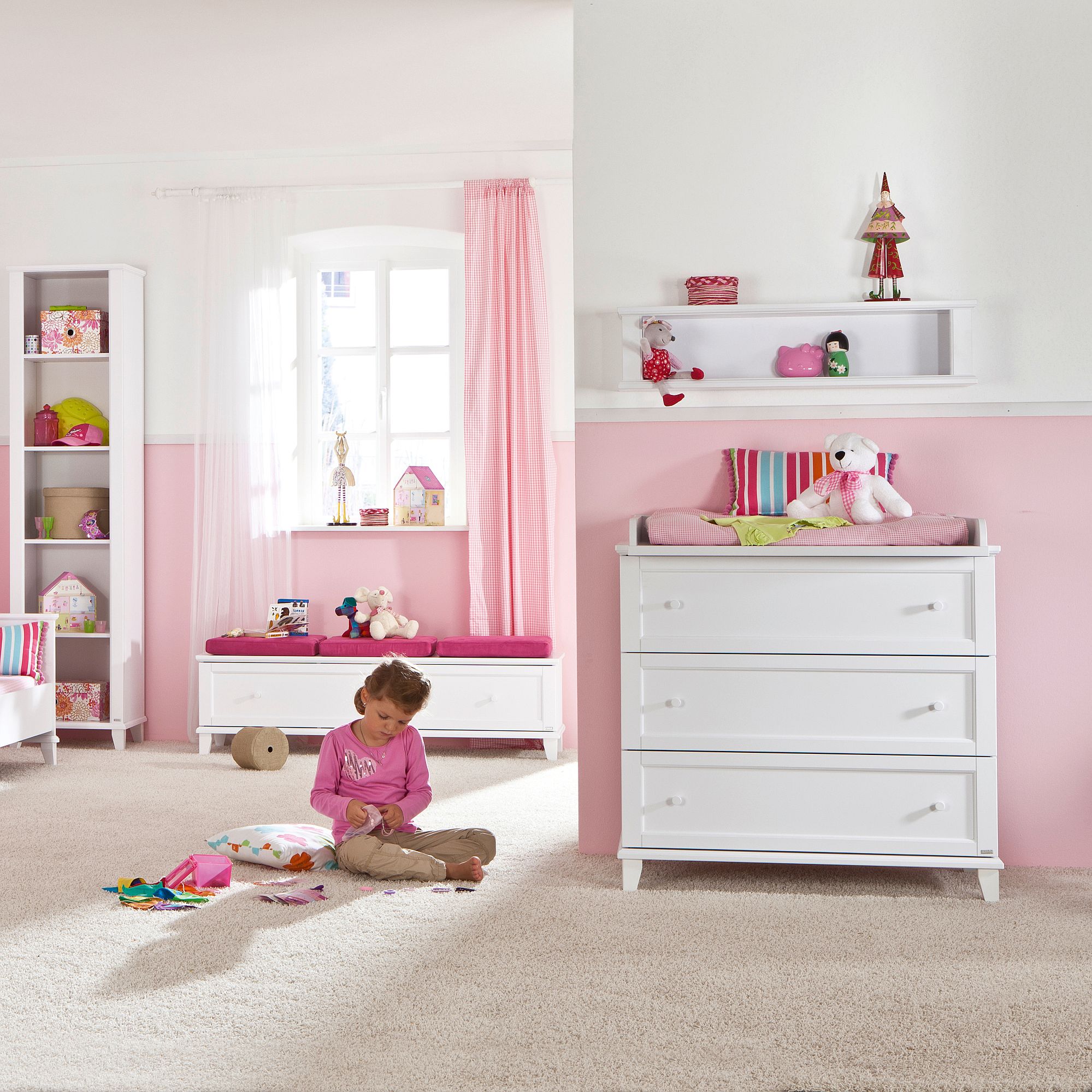 Young girl playing on floor in a pink and white childrens bedroom with toys.