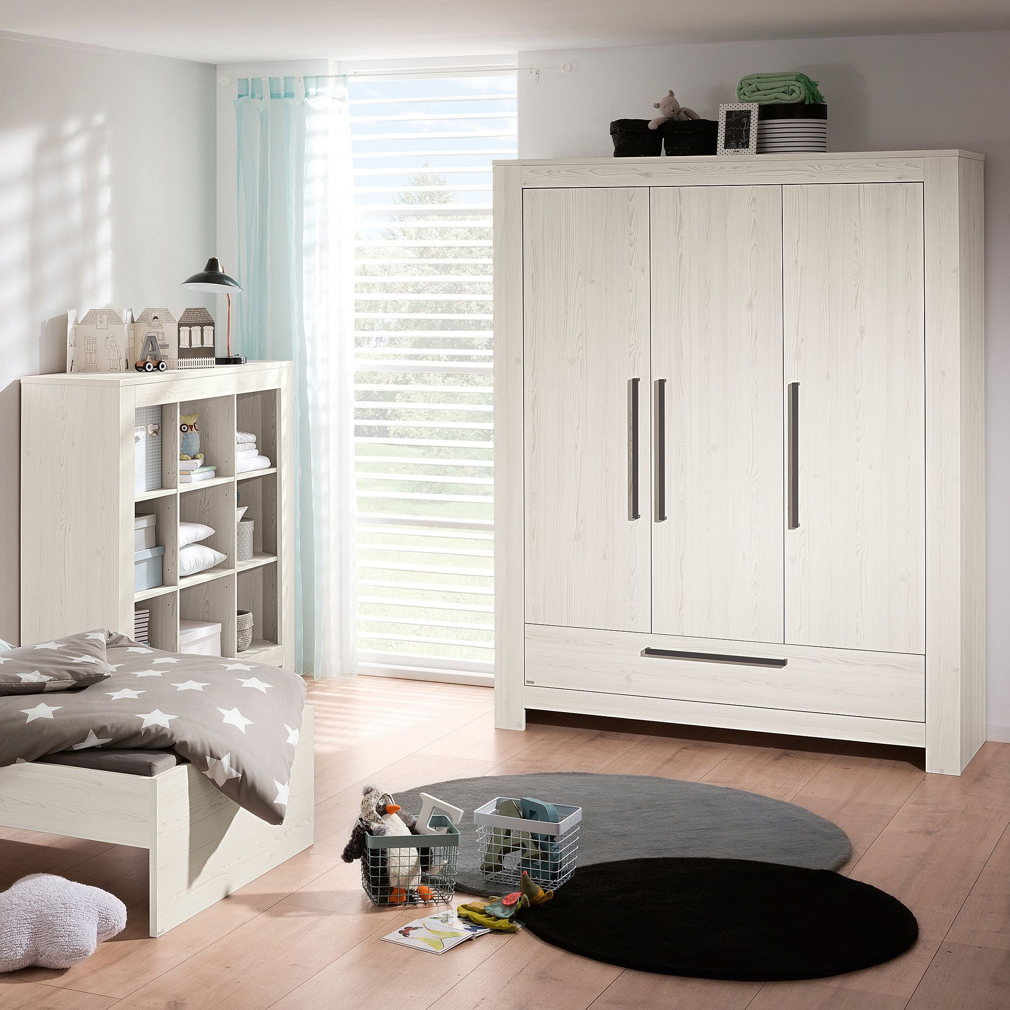 Drehtürenschrank Laslo mit 3 Türen und 1 Schublade Helles, modernes Kinderzimmer mit weißen Möbeln und Spielzeug auf dem Boden.