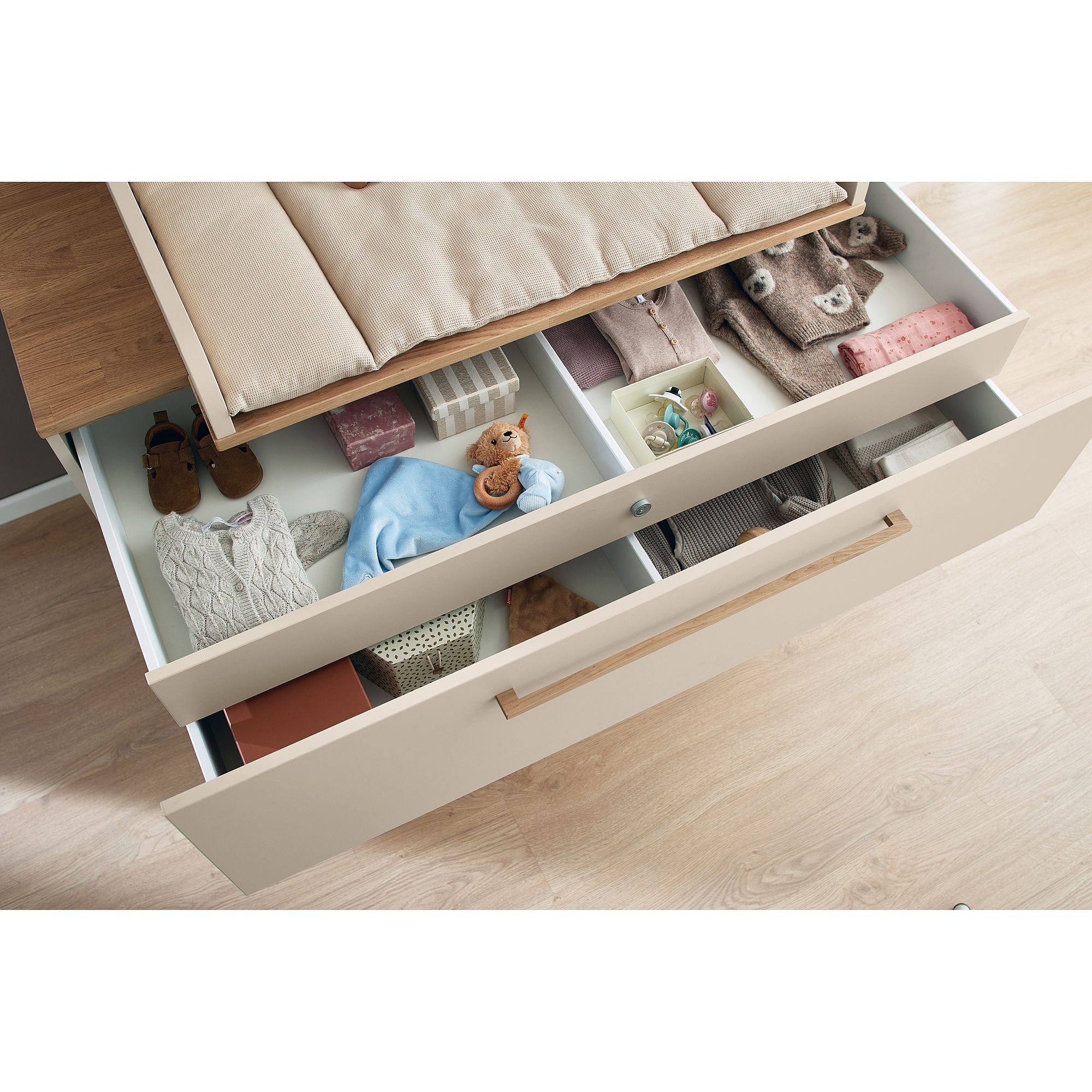 Offene Kommodenschublade mit ordentlich organisierter Babykleidung, Spielzeug und Zubehör.