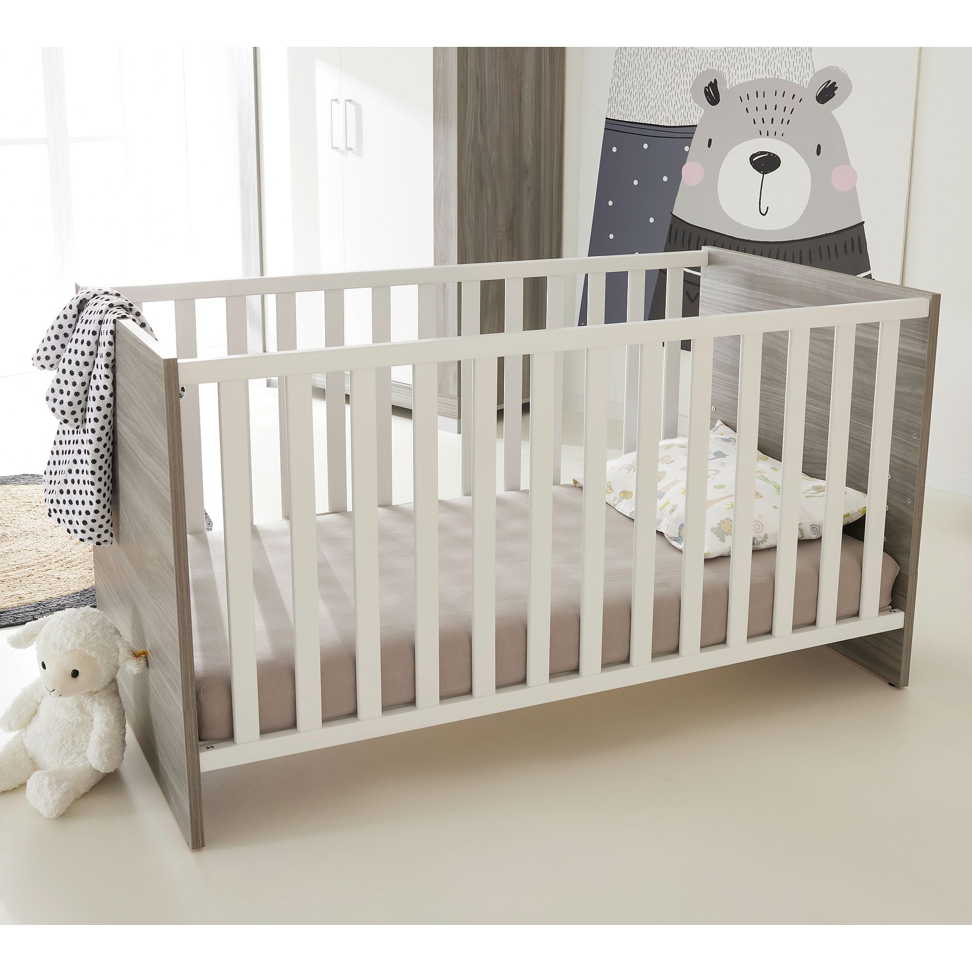 Modernes Babybett mit weißem und grauem Rahmen, Bettzeug und ausgestopftem Bär daneben.