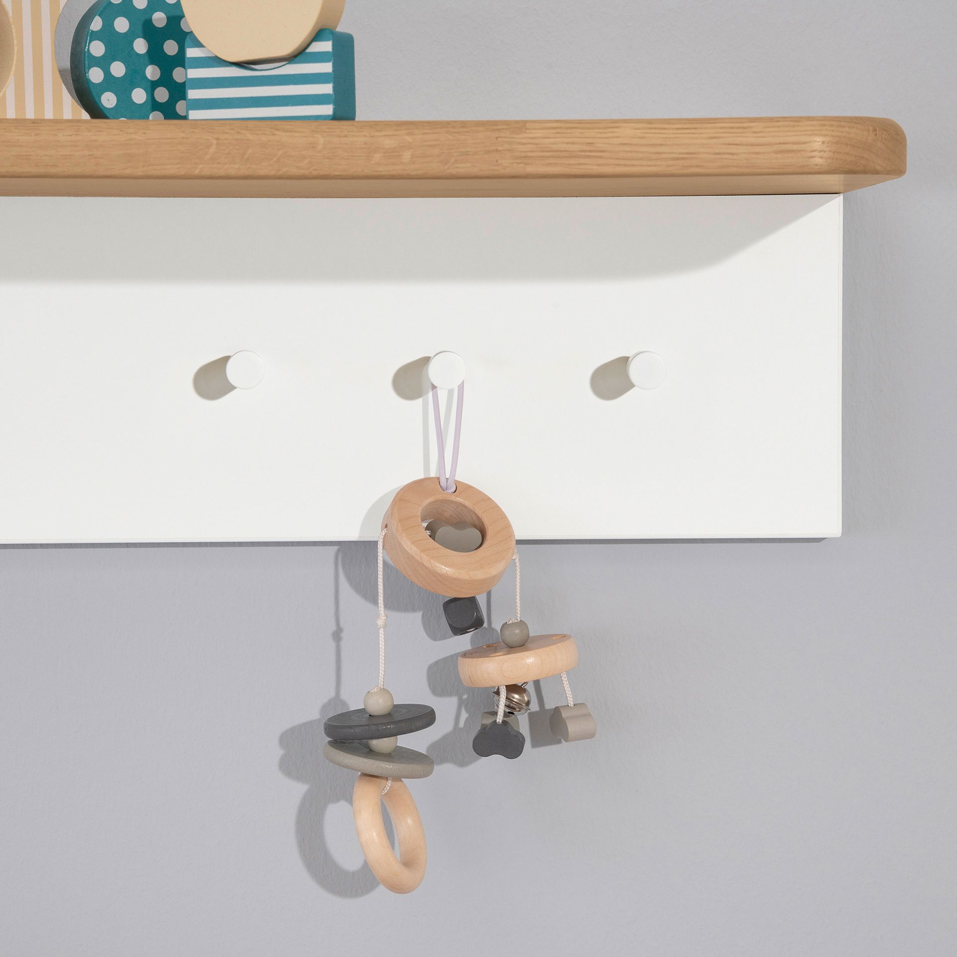 Babyspielzeug aus Holz hängt an weißen Haken unter einem Holzregal.