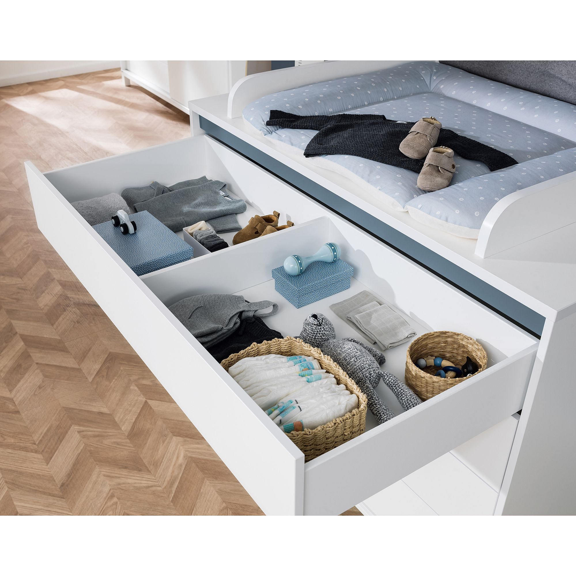 Offene Schublade mit ordentlich organisierter Babykleidung, Windeln und Körben.