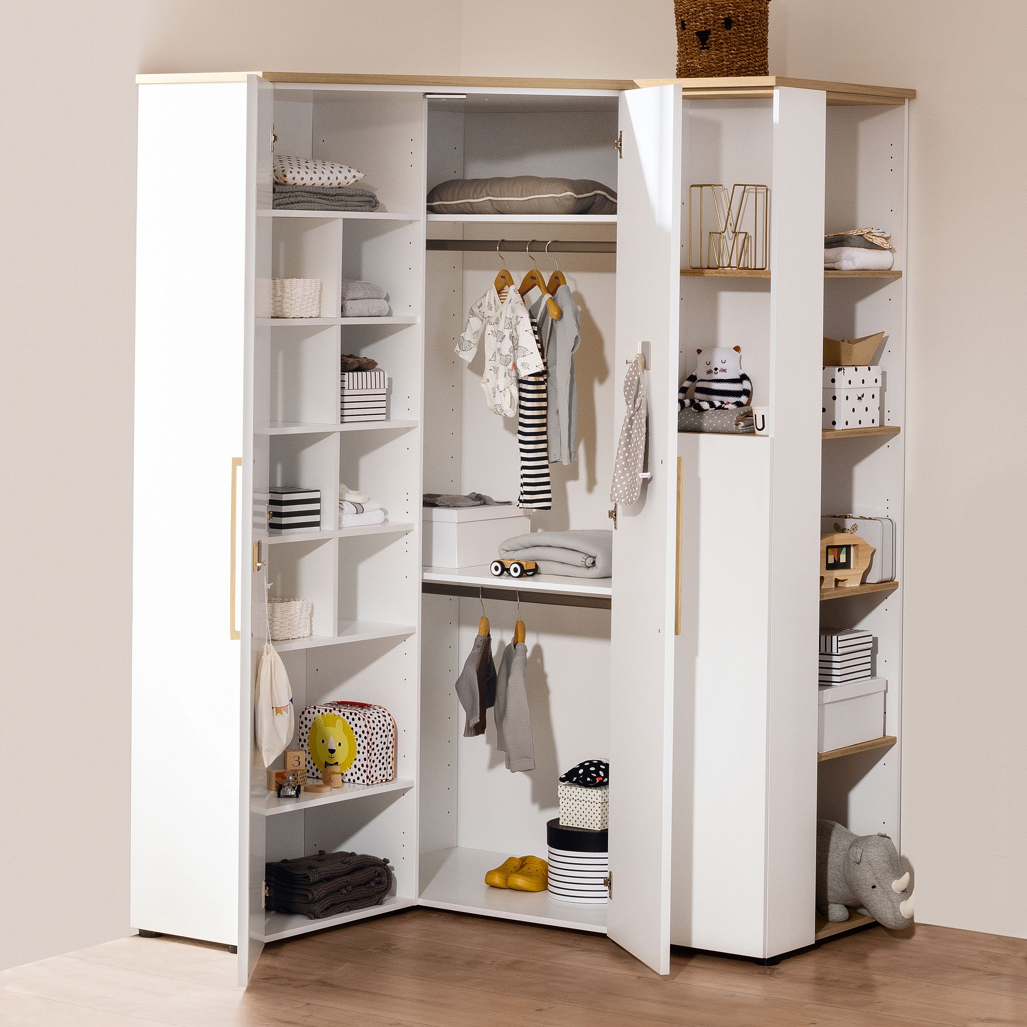Offener weißer Eckschrank mit Regalen, darin hängende Kleidung, Körbe und Spielzeug.