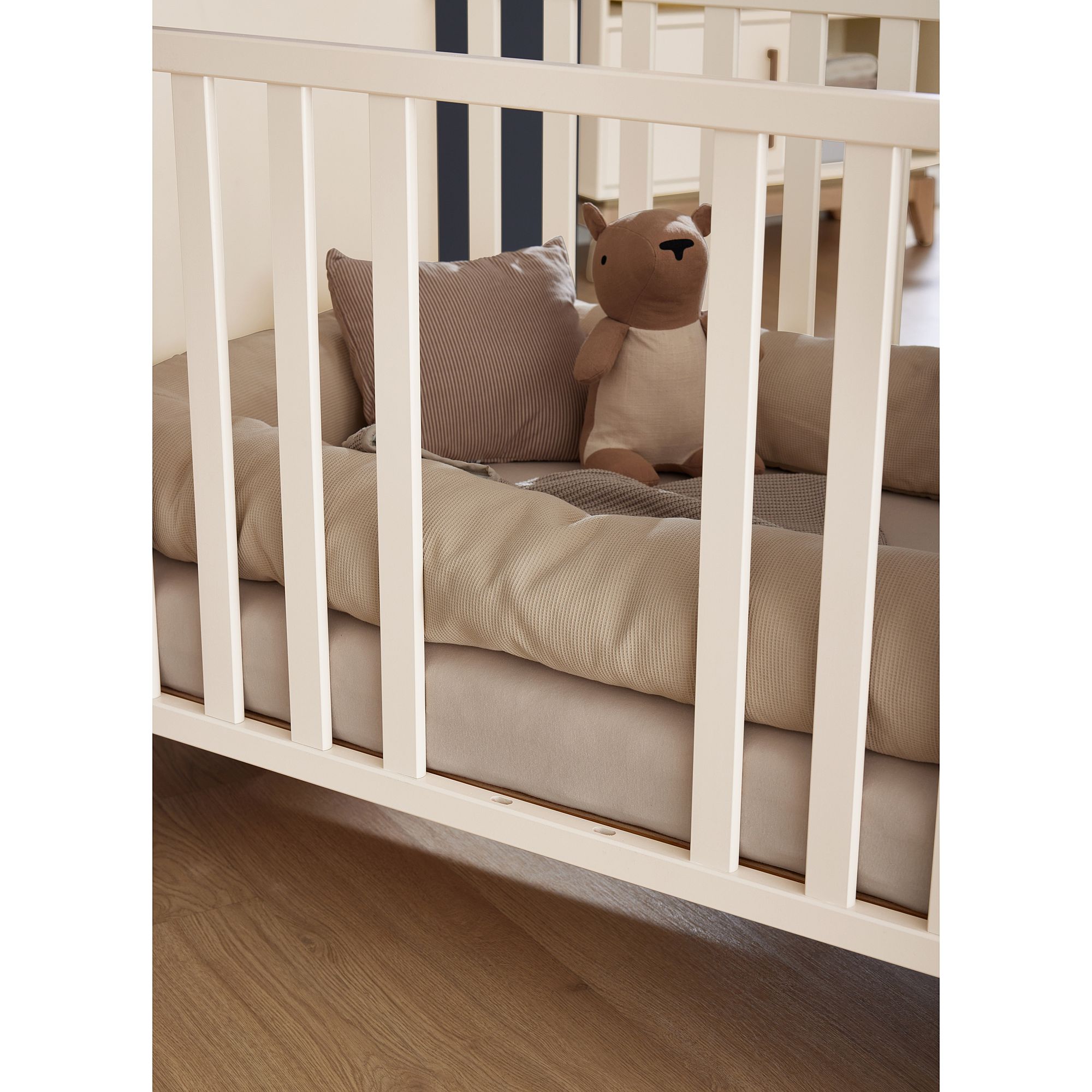 Ein ausgestopfter Bär und Kissen in einem weißen Babybettchen auf einem Holzboden.
