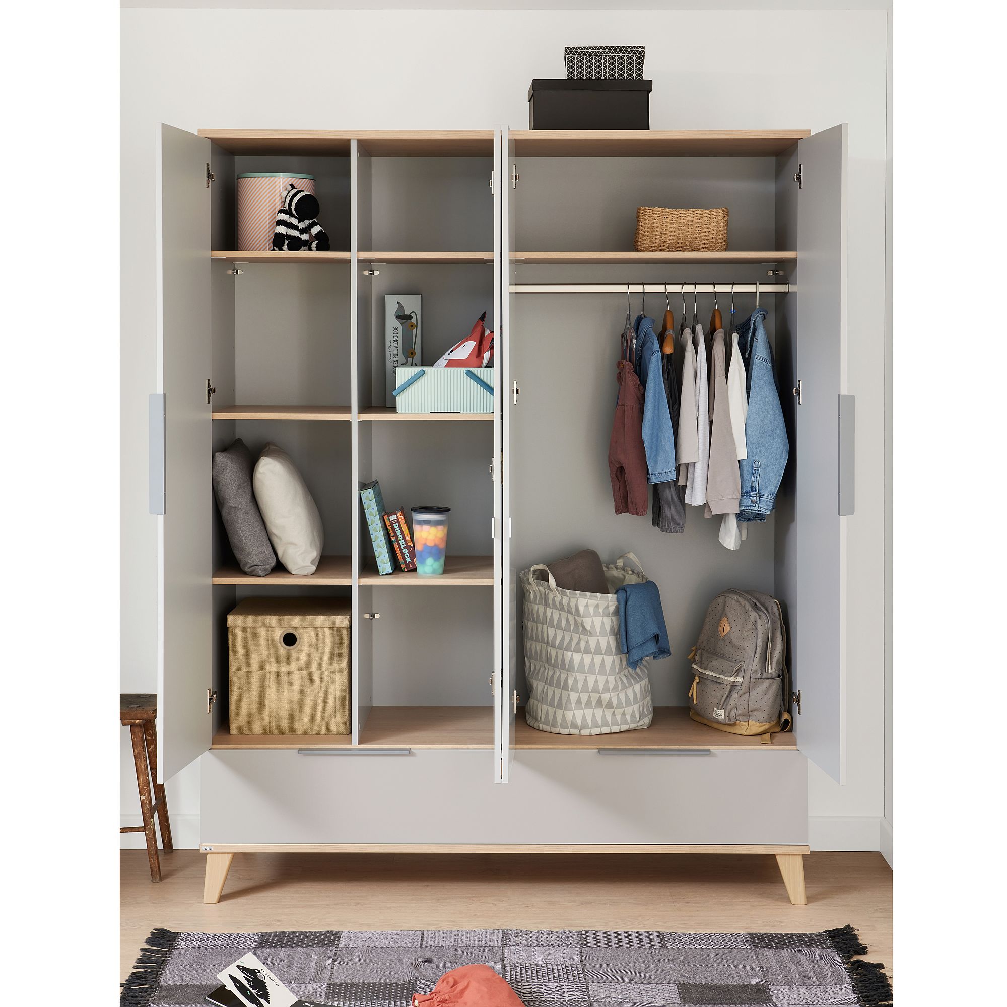 Offener Kleiderschrank mit Einlegeböden, hängenden Kleidungsstücken, Körben und Kissen im Inneren.