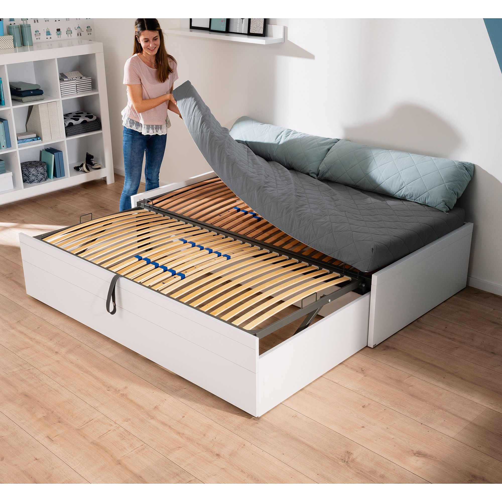 Eine Frau hebt eine Matratze auf einem weißen ausziehbaren Stauraumbett in einem modernen Schlafzimmer an.