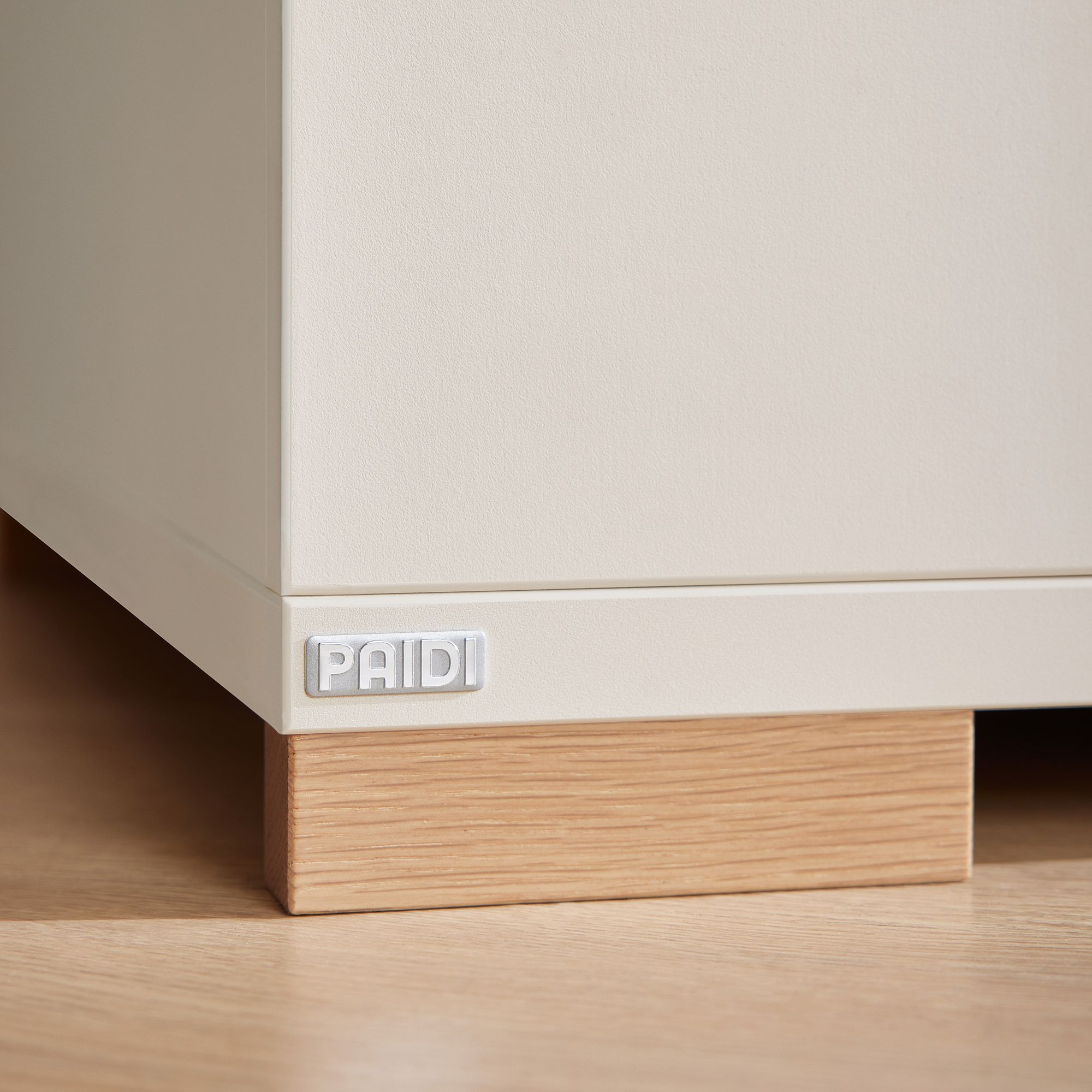 Nahaufnahme einer weißen Schrankecke mit einem PAIDI-Etikett und einem Holzsockel.