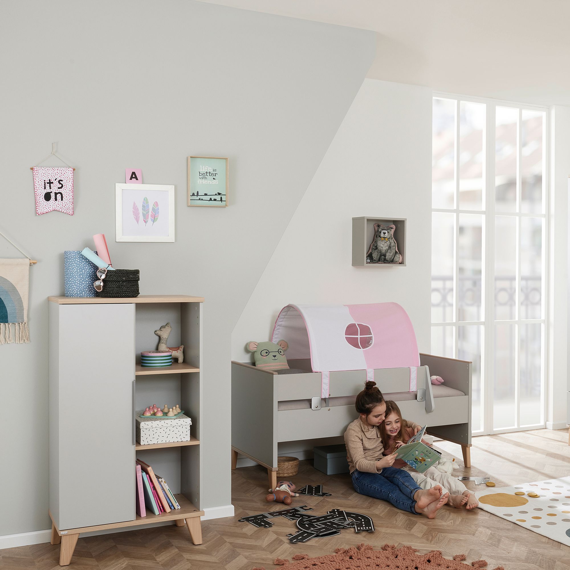 Eine Frau und ein Kind lesen gemeinsam auf dem Boden in einem gemütlichen, modernen Kinderzimmer.
