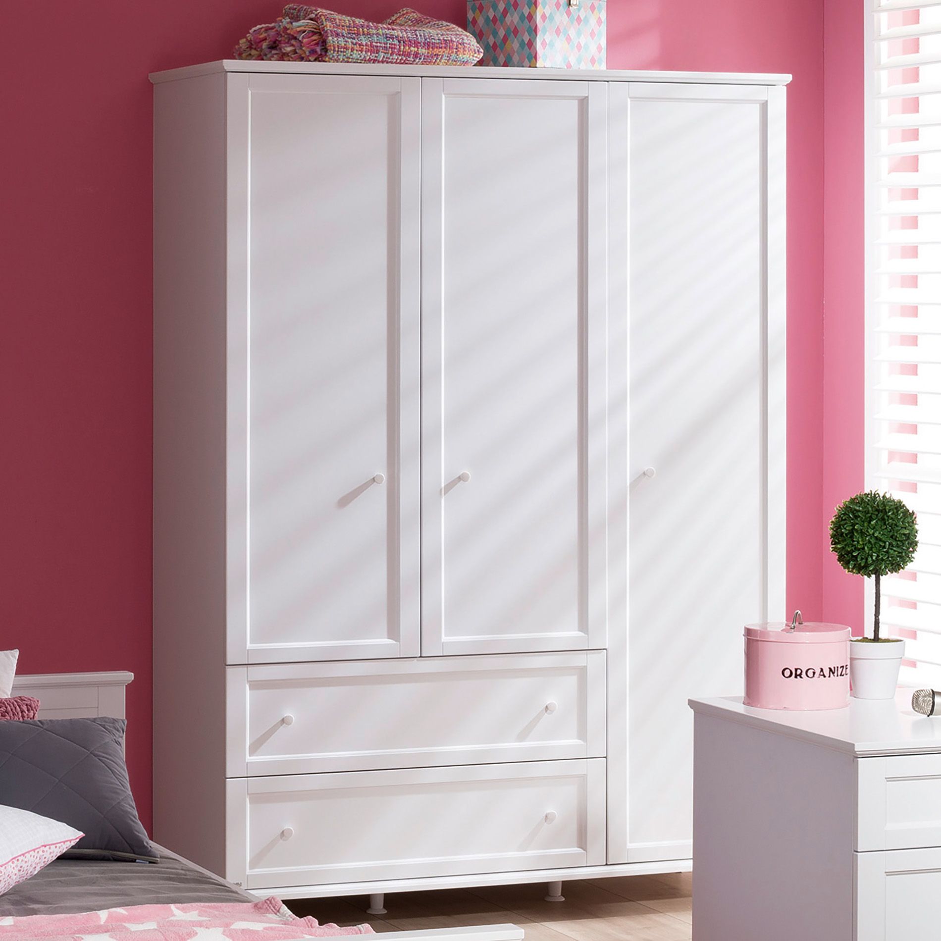 White wardrobe with two drawers in a pink bedroom, sunlight streaming in.