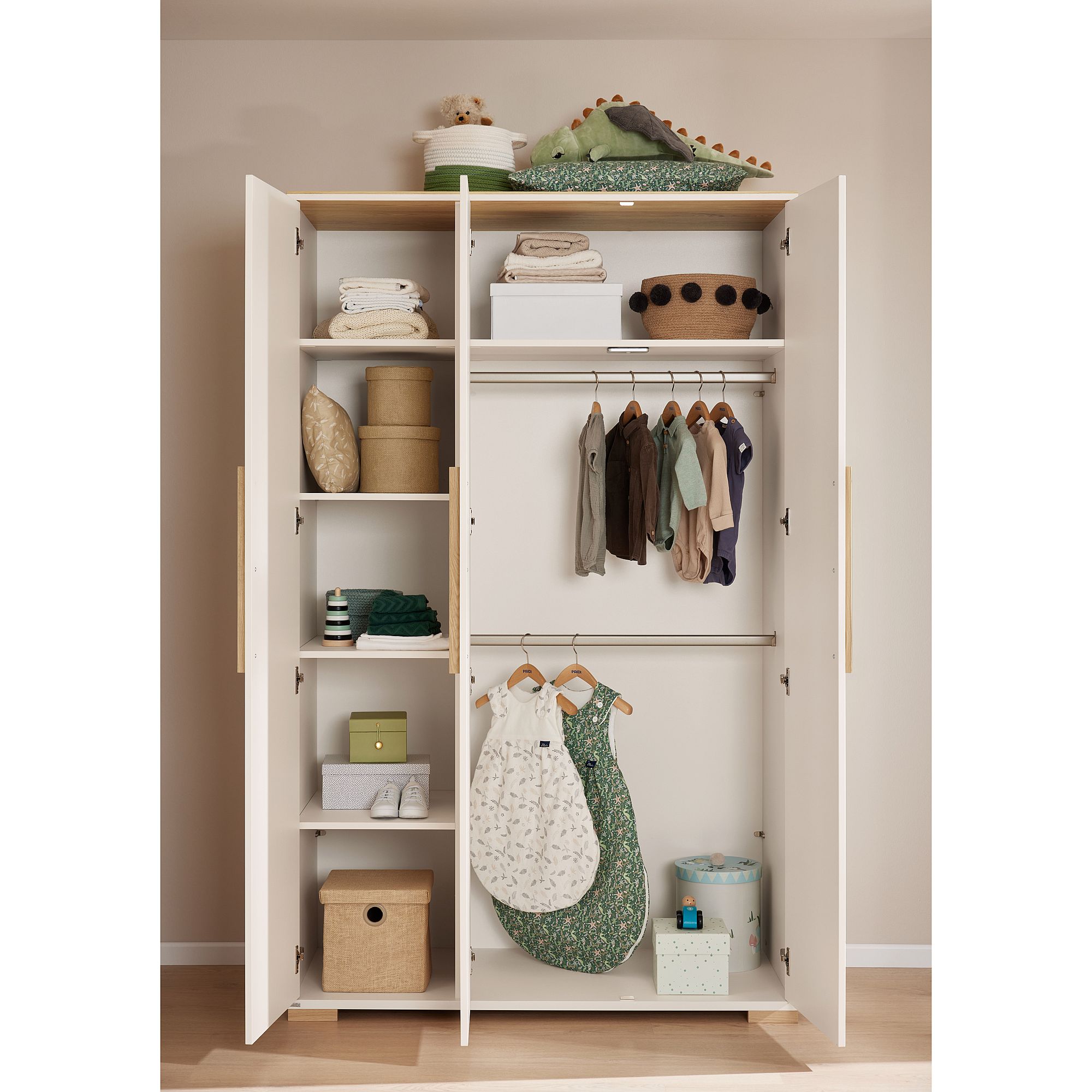 Offener Kleiderschrank mit ordentlich geordneter Babykleidung, Körben und Kuscheltieren darin.