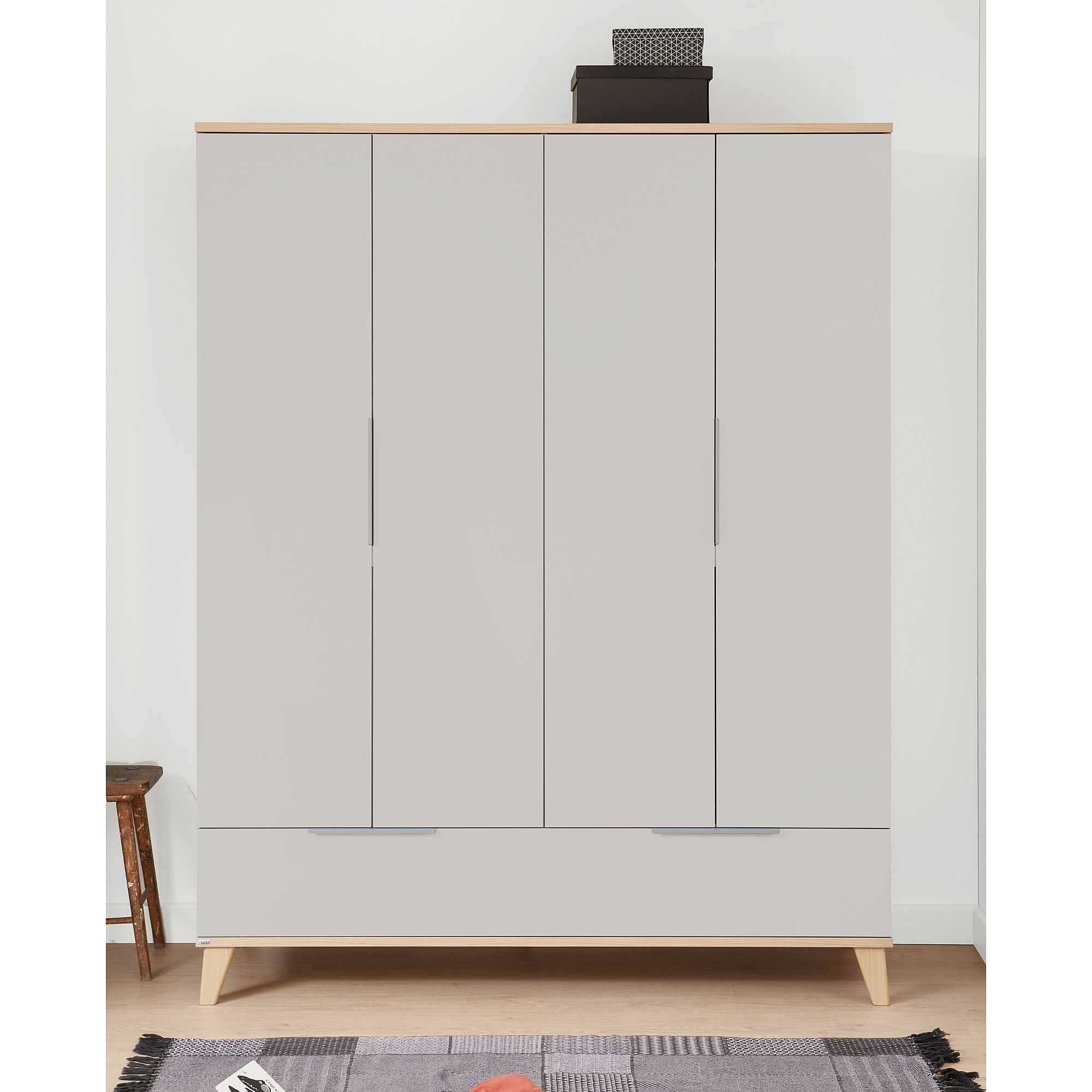 Beigefarbener Schrank mit Holzbeinen, einer Kiste darauf und einem Hocker daneben.