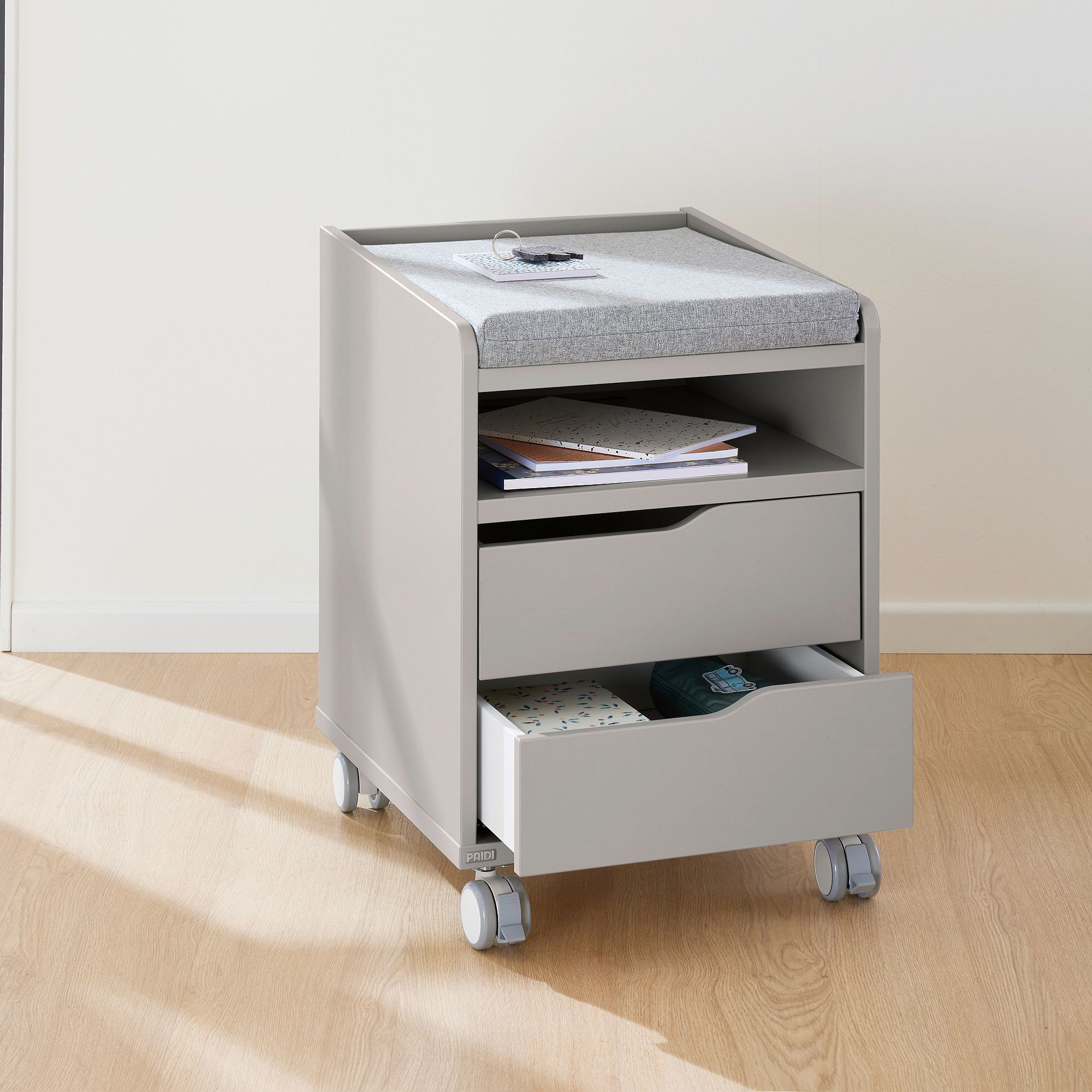 Rollcontainer  mit 2 Schubladen in Kieselgrau Grauer rollender Aufbewahrungswagen mit Schubladen, Kissen und Büchern im Inneren.