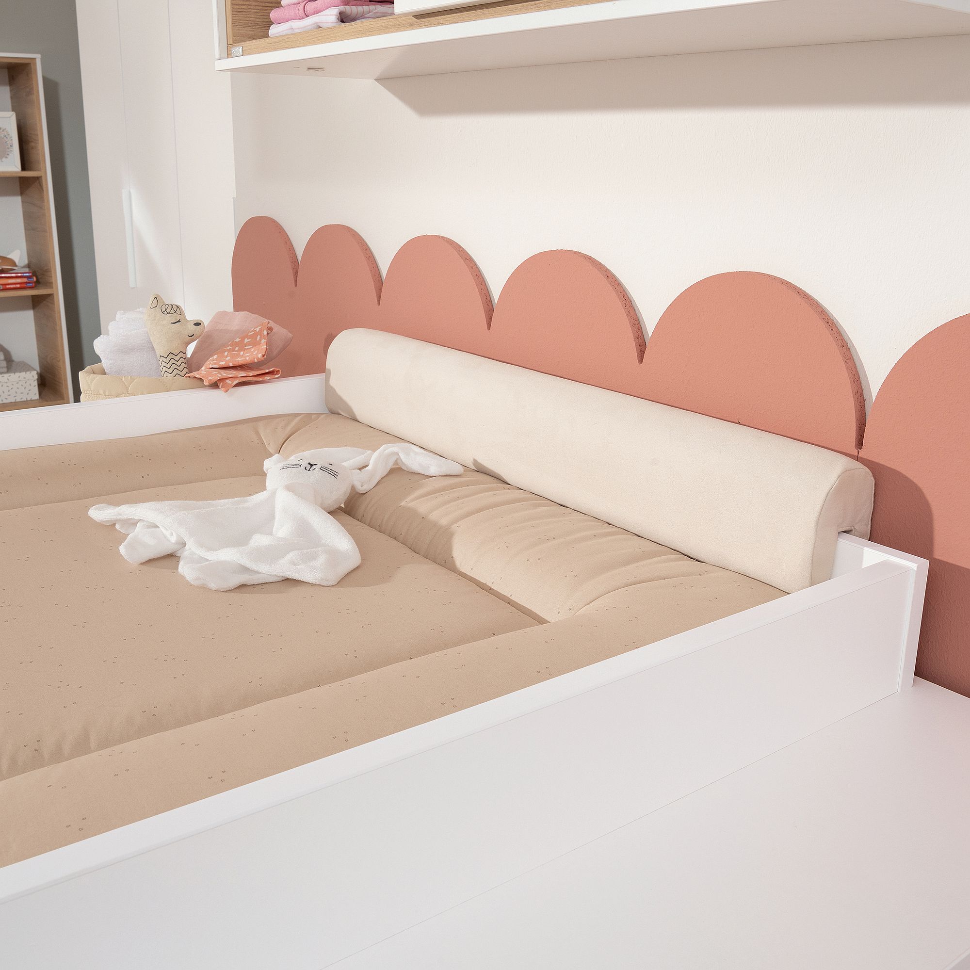 Beige changing pad on white table with pink scalloped wall decor behind it.