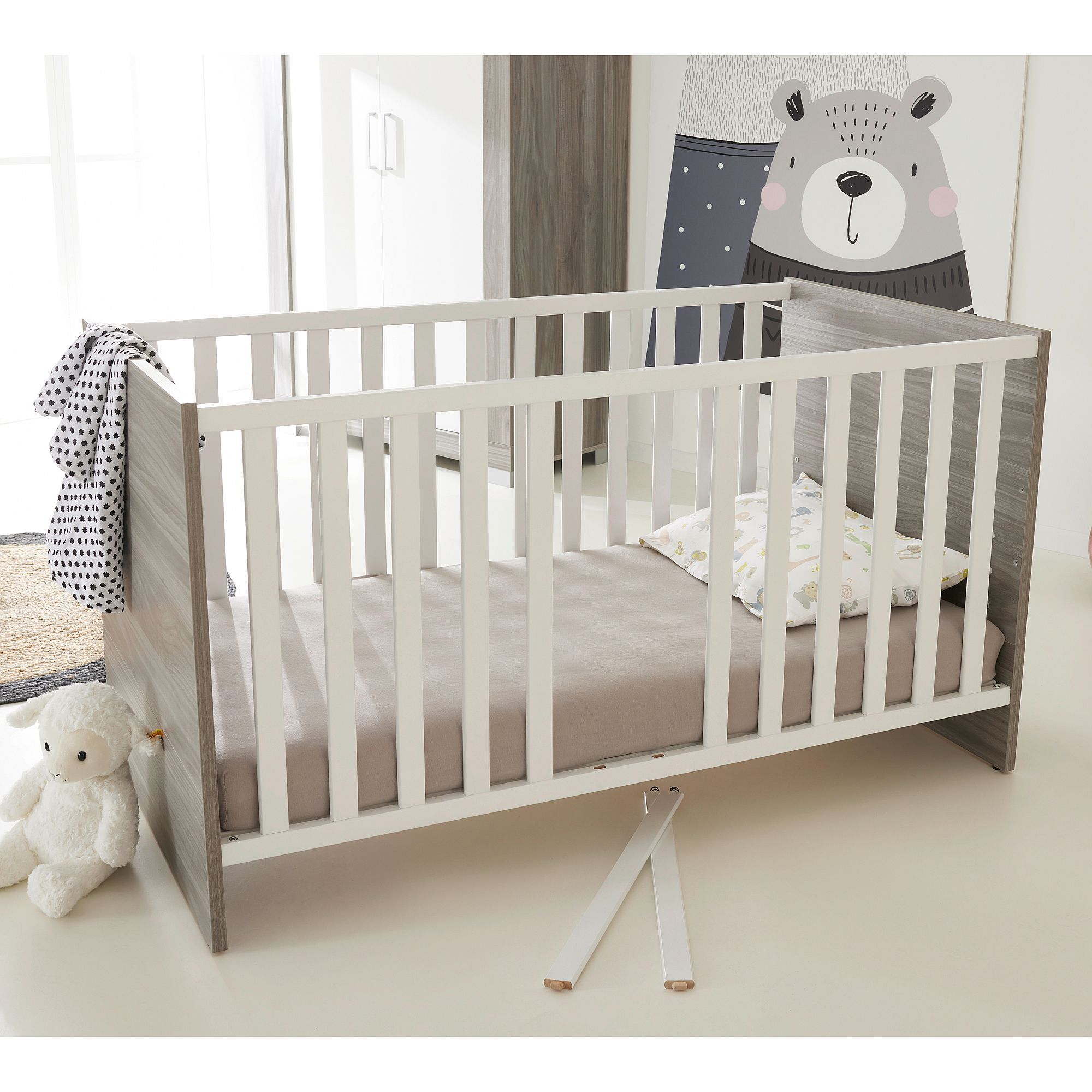 Ein modernes Kinderbett mit einem fehlenden Geländer, einem Teddybär und einer Bärenkunst im Hintergrund.