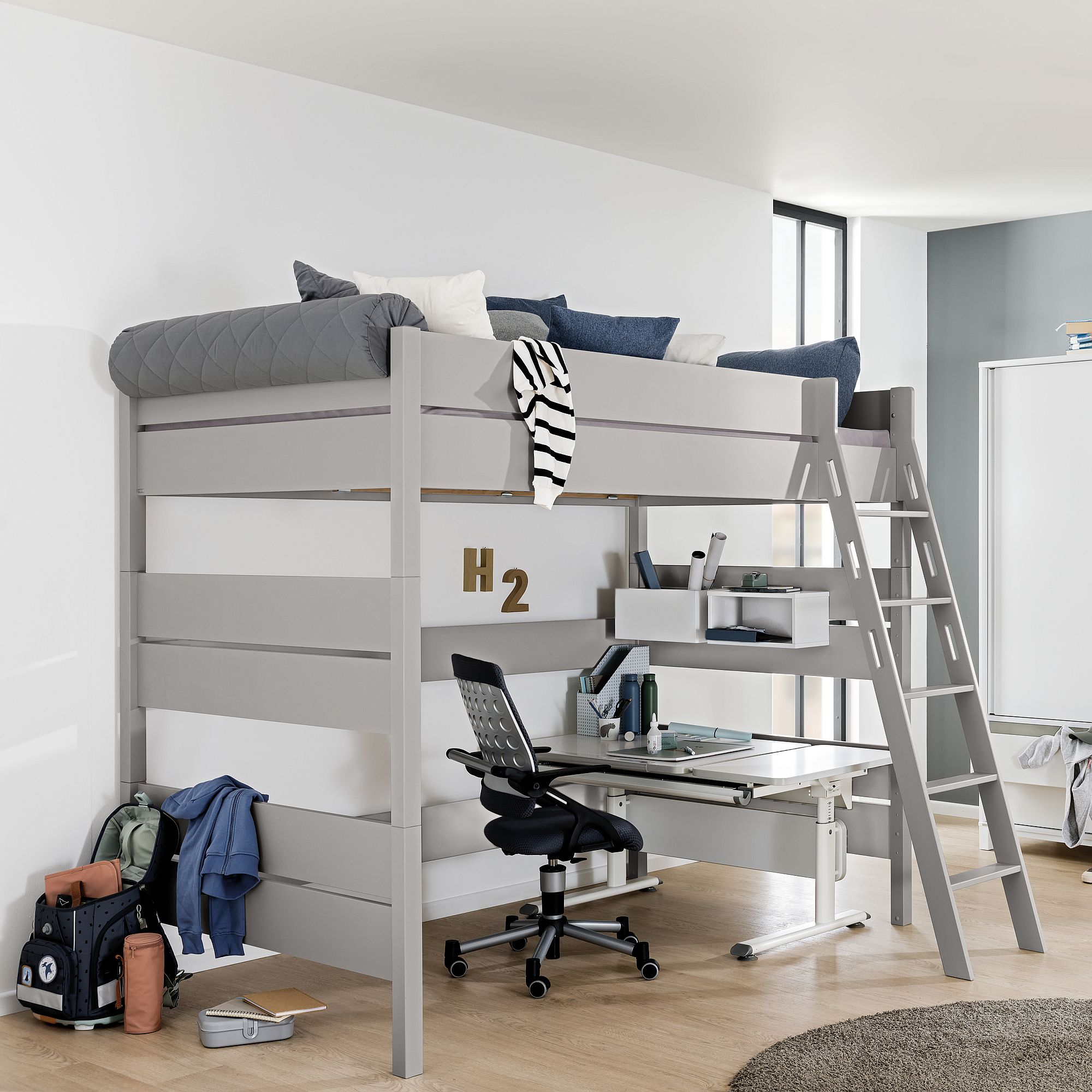 Graues Hochbett mit Leiter, Schreibtisch und Stuhl darunter in einem modernen Schlafzimmer.