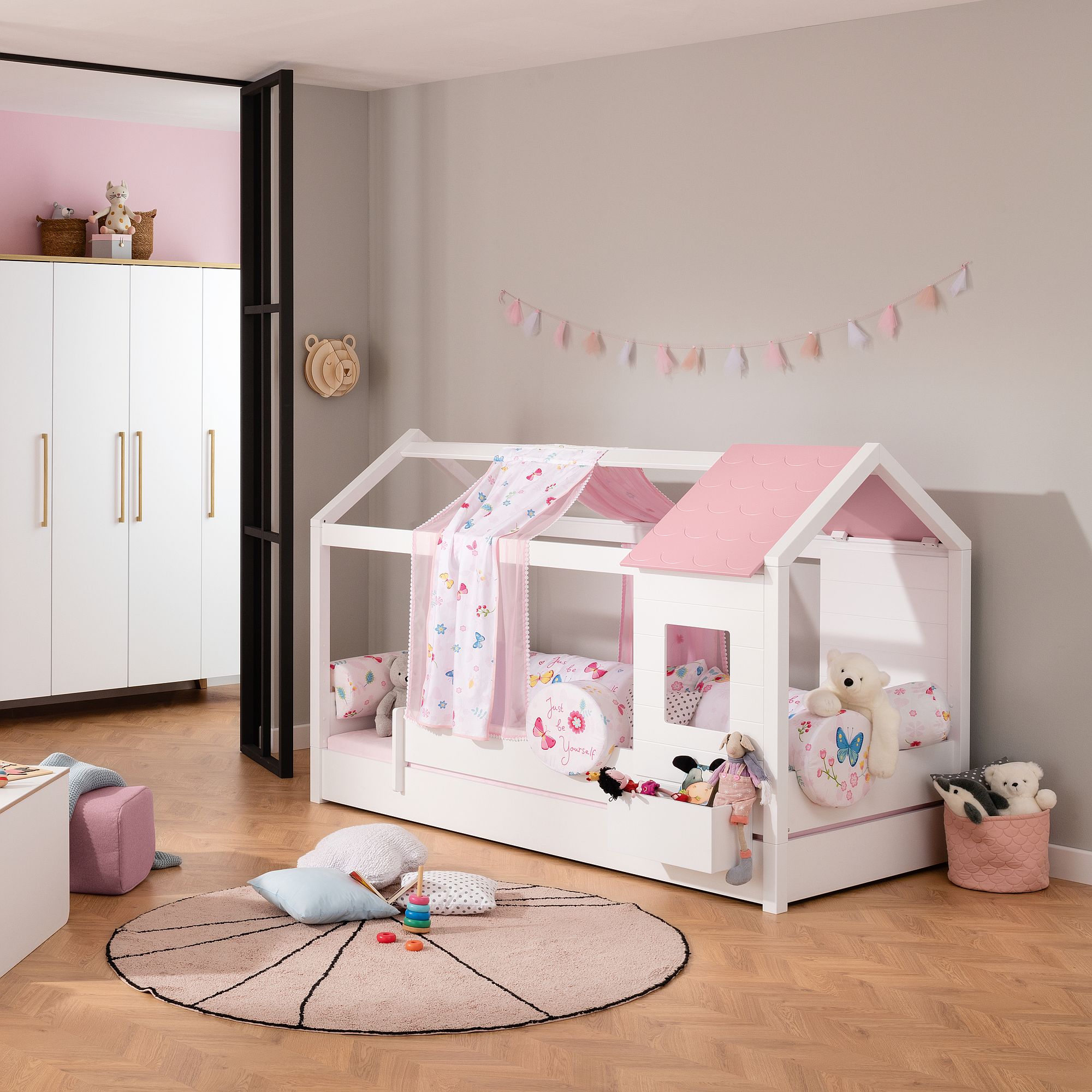 Kinderzimmer mit einem hausförmigen Bett, rosa Dekoration, Spielzeug und Kissen.
