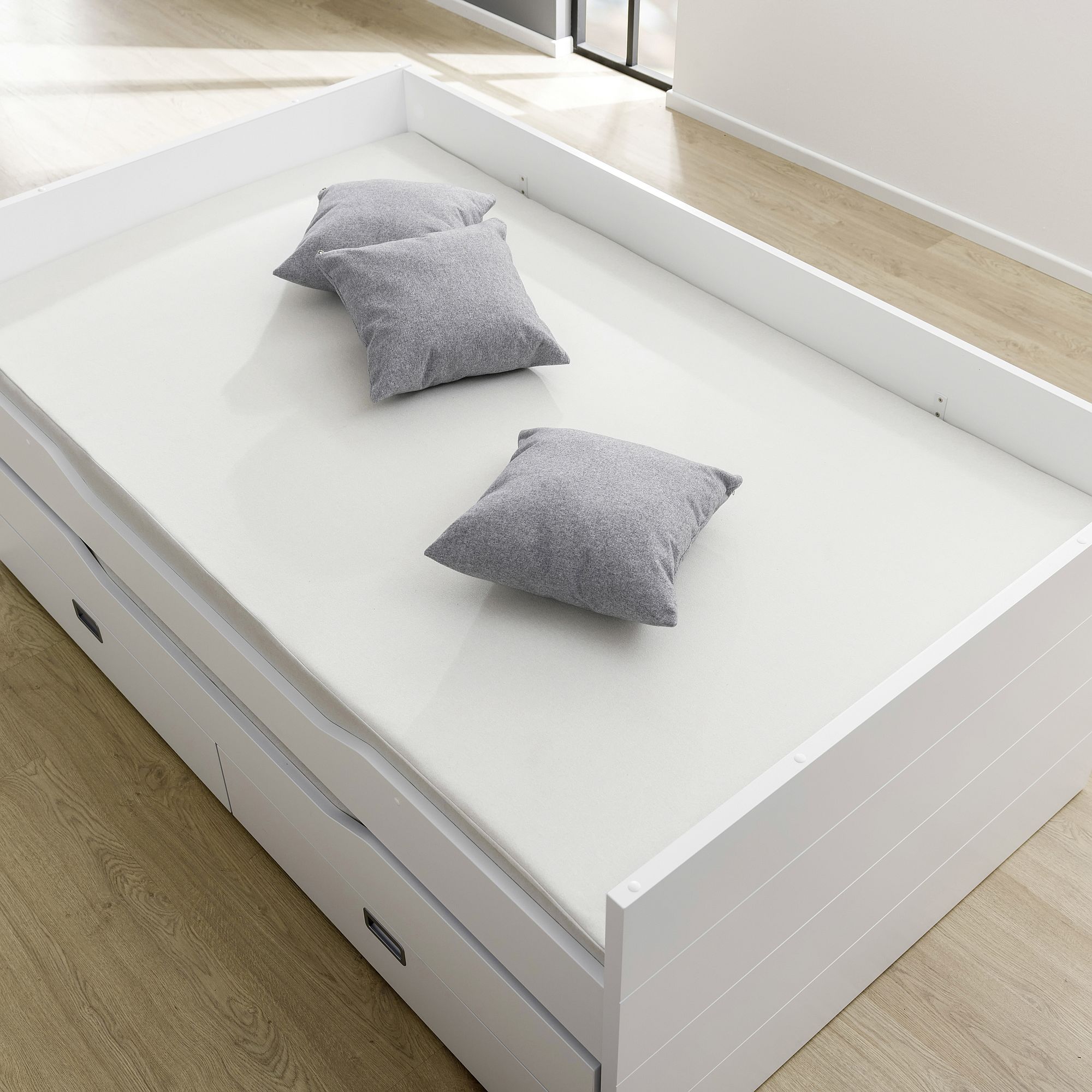 White daybed with three gray pillows on a white mattress in a bright room.