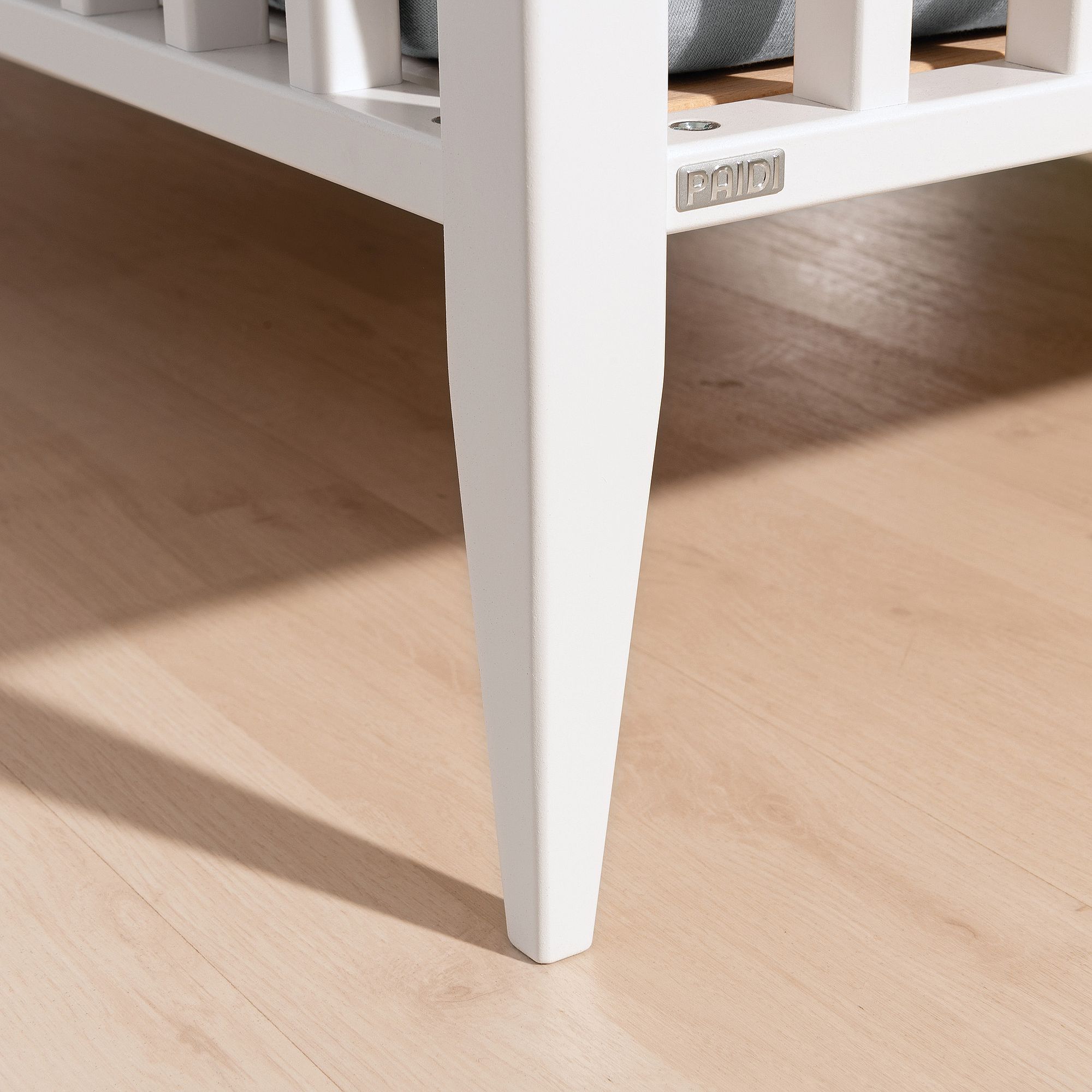 Babybett Felie 70 x 140 cm Nahaufnahme eines weißen Krippenbeins auf einem hellen Holzboden.