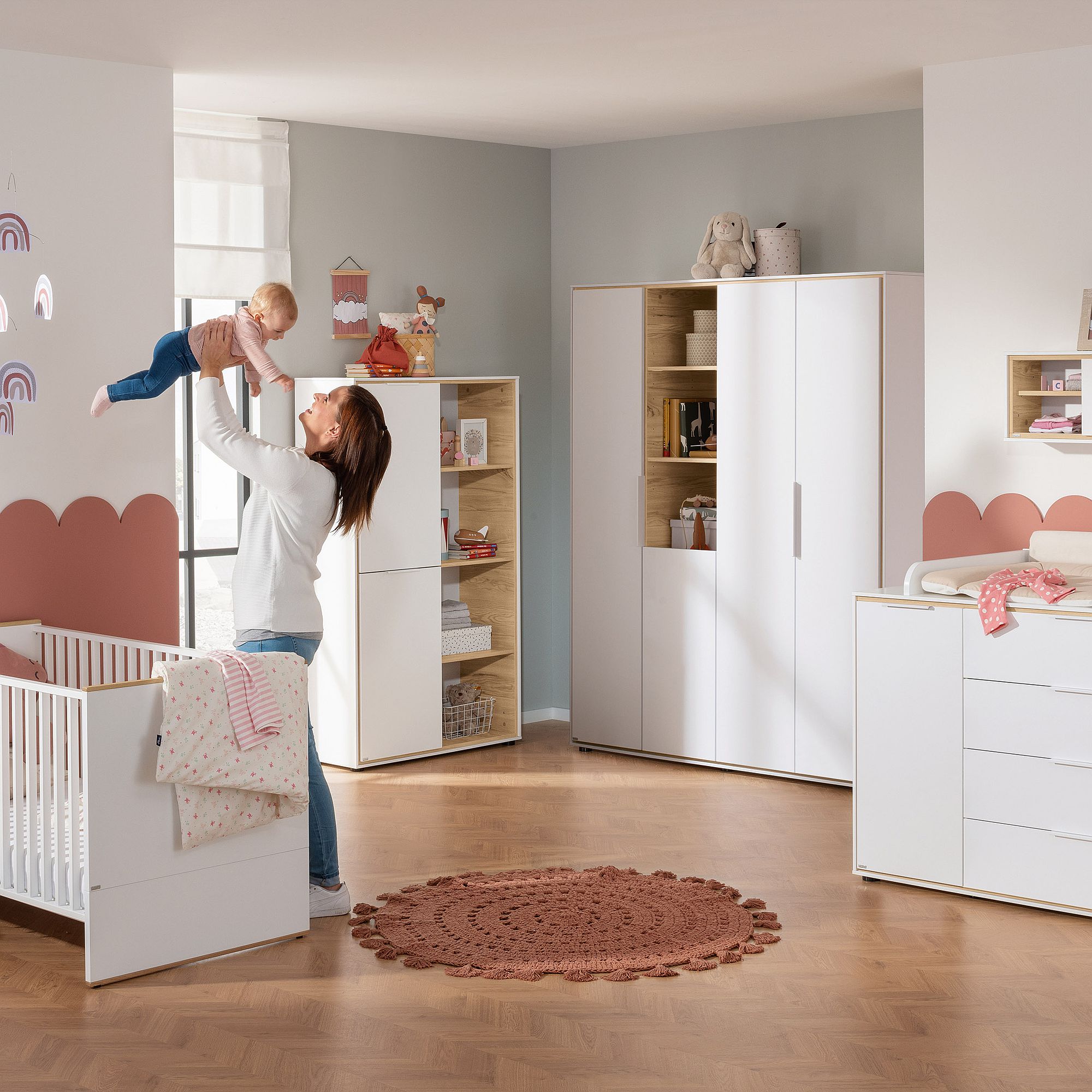 Eine Frau hebt ein Baby in einem modernen, pastellfarbenen Kinderzimmer hoch.