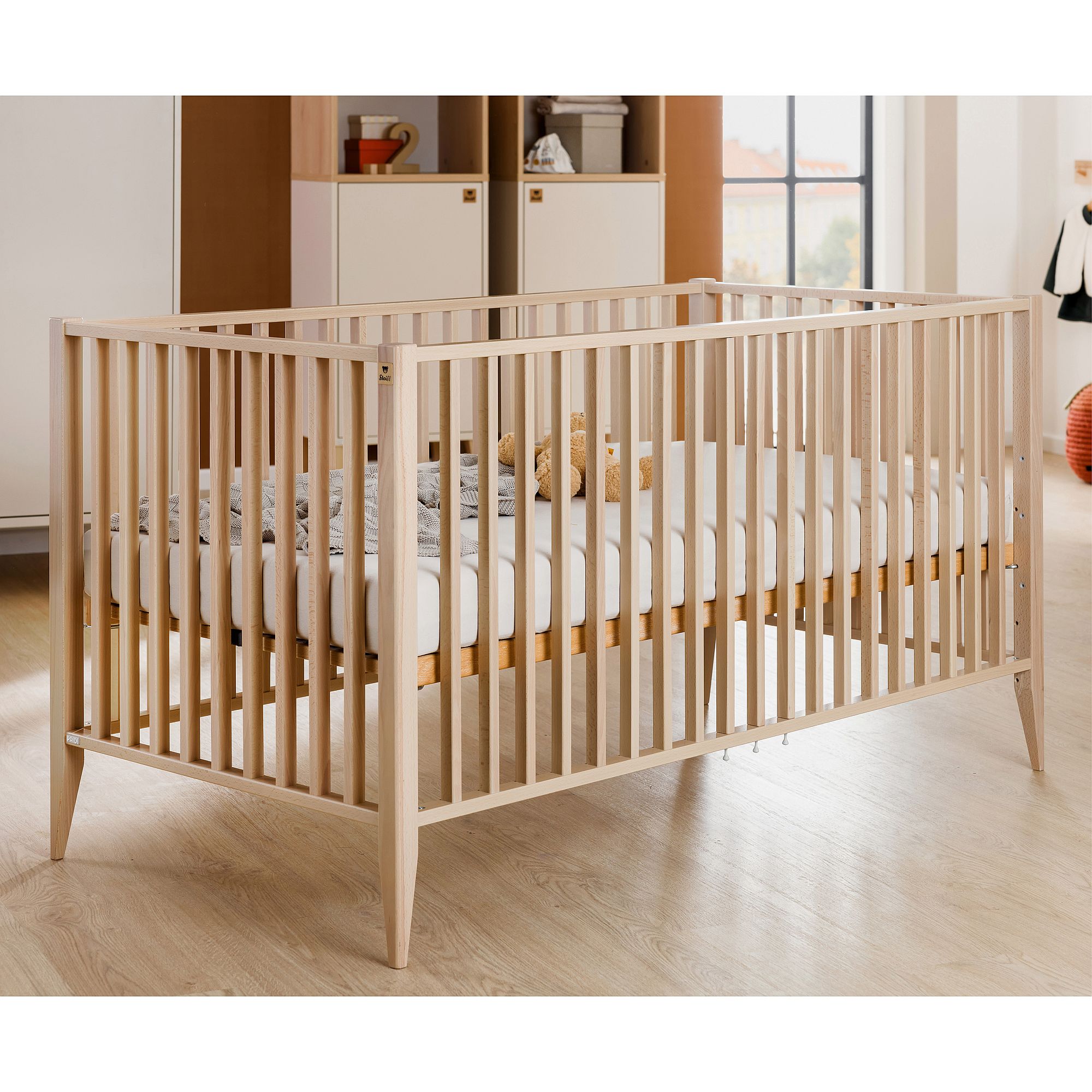 Babybett aus Holz mit weißer Matratze in einem hellen, modernen Kinderzimmer.