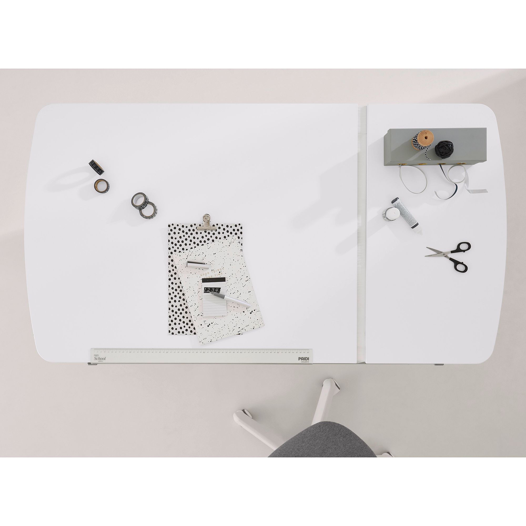 White desk with stationery, papers, scissors, tape, and a gray chair visible.