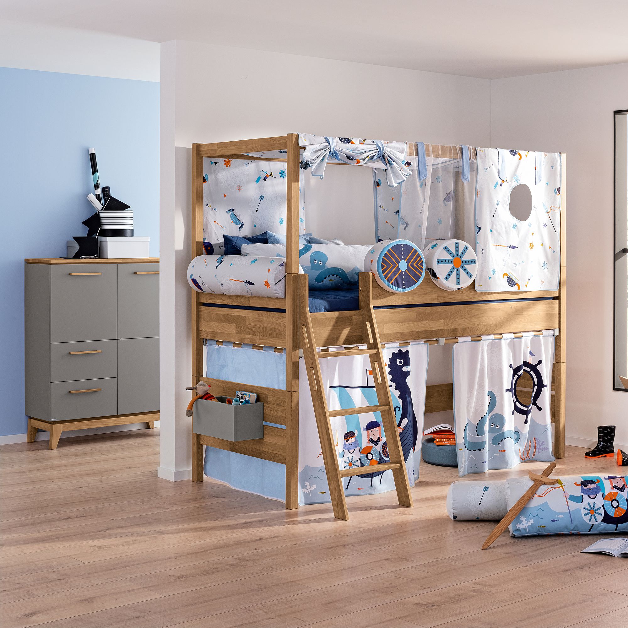 Ein Kinder-Etagenbett mit verspielter Bettwäsche im maritimen Stil und einer Kommode daneben.