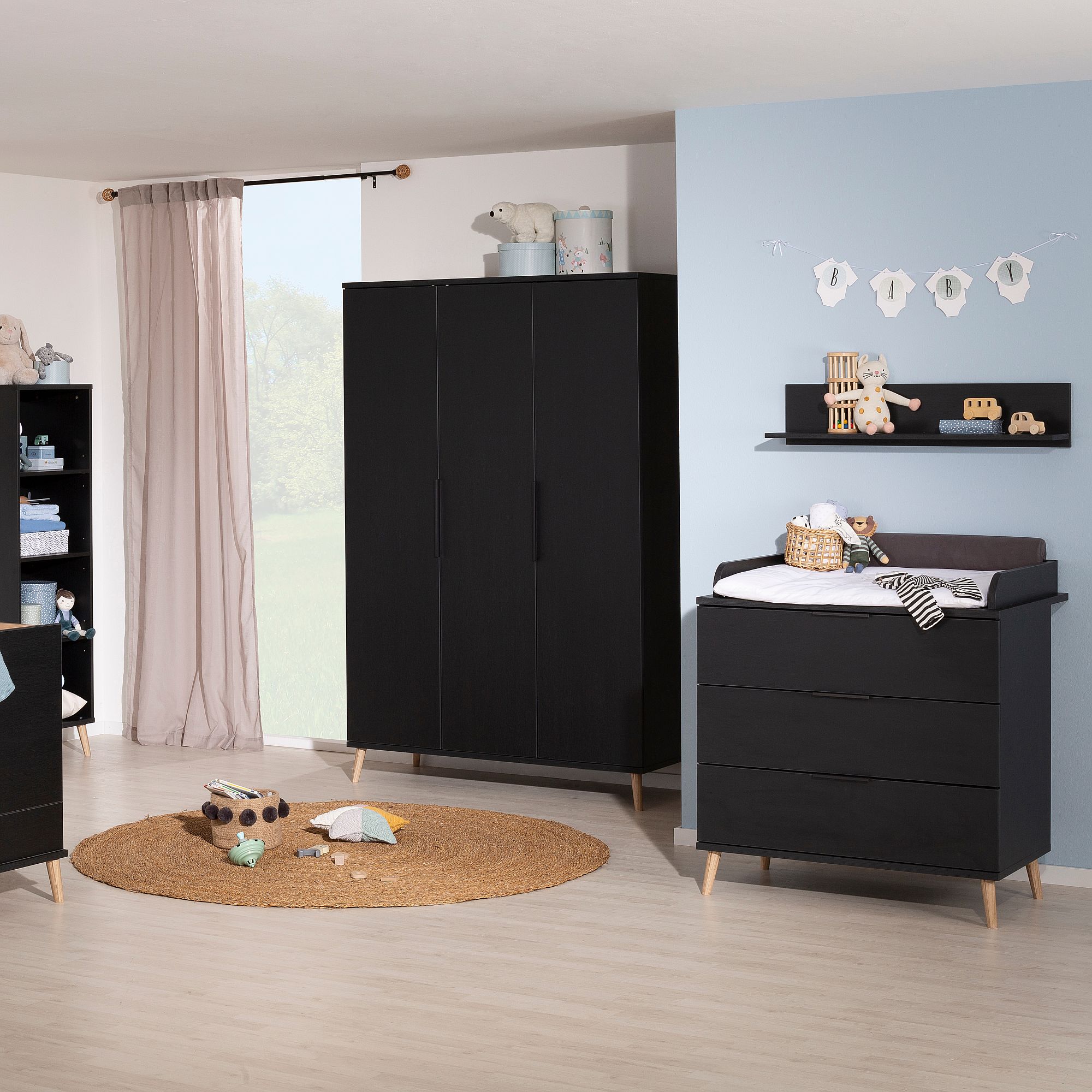 Modernes Kinderzimmer mit schwarzen Möbeln, Spielzeug auf einem runden Teppich und einer blauen Akzentwand.