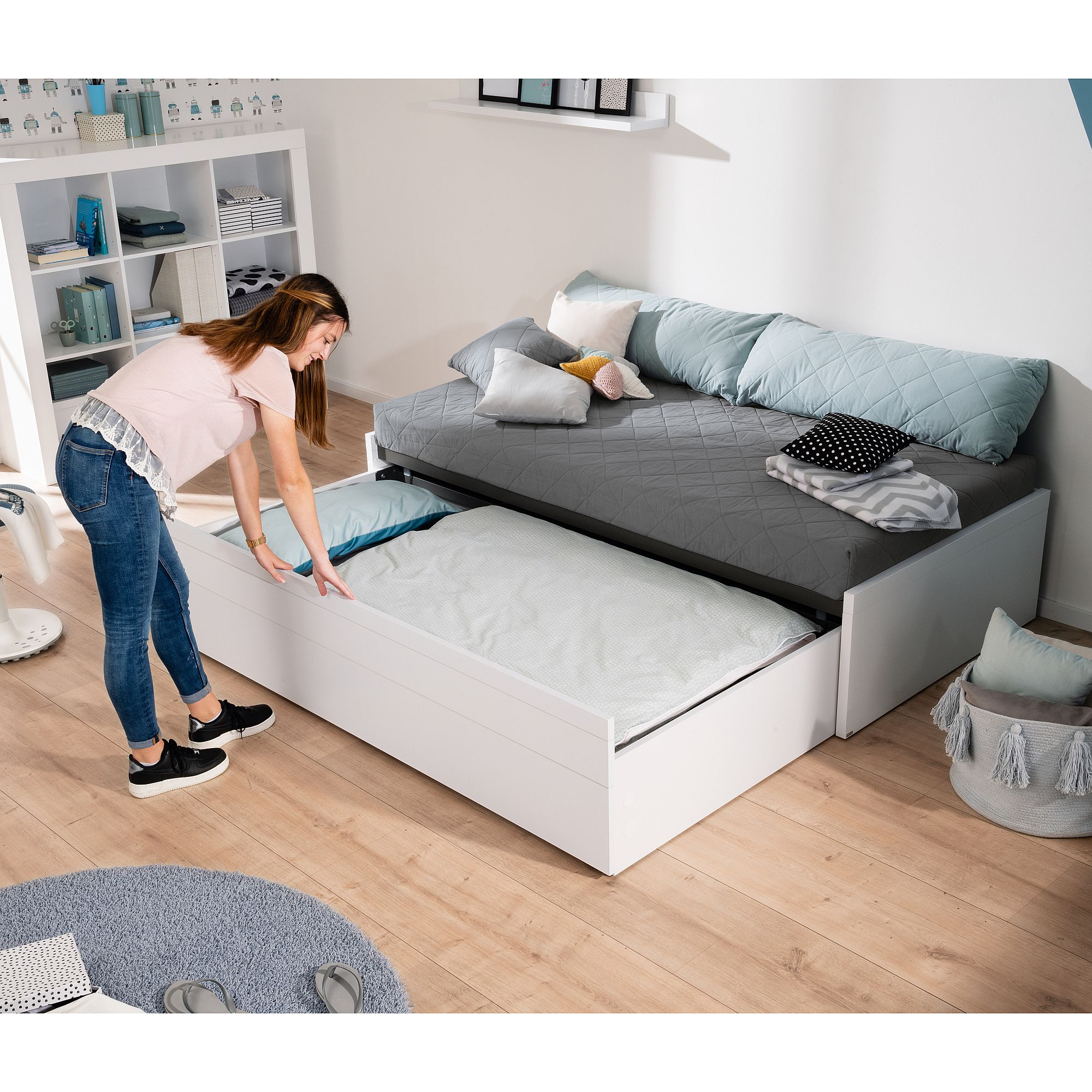 Frau, die in einem modernen, aufgeräumten Schlafzimmer ein Rollbett auszieht.