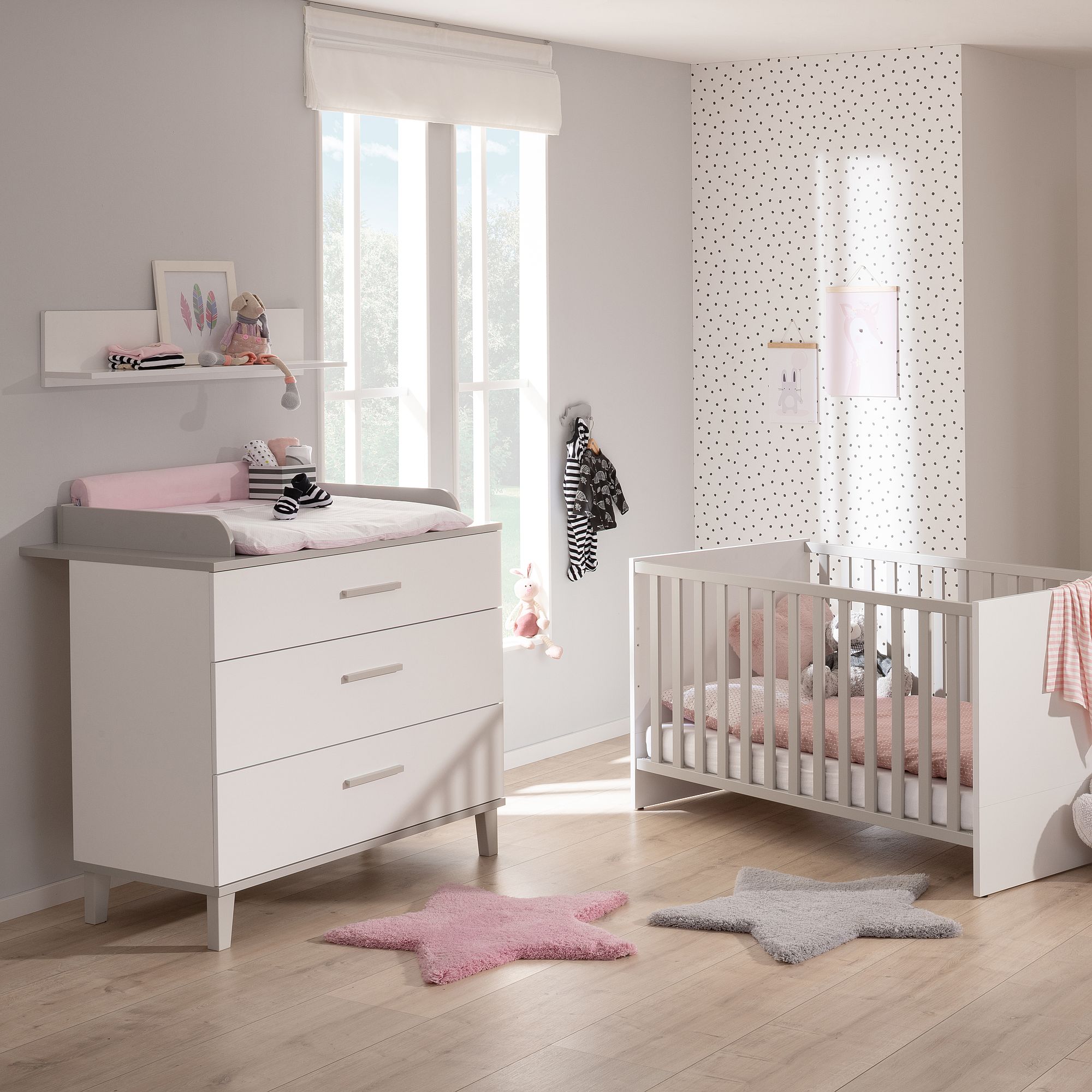 Modernes Kinderzimmer mit einem Kinderbett, einer Kommode und rosa und grauen Sternenteppichen auf dem Boden.