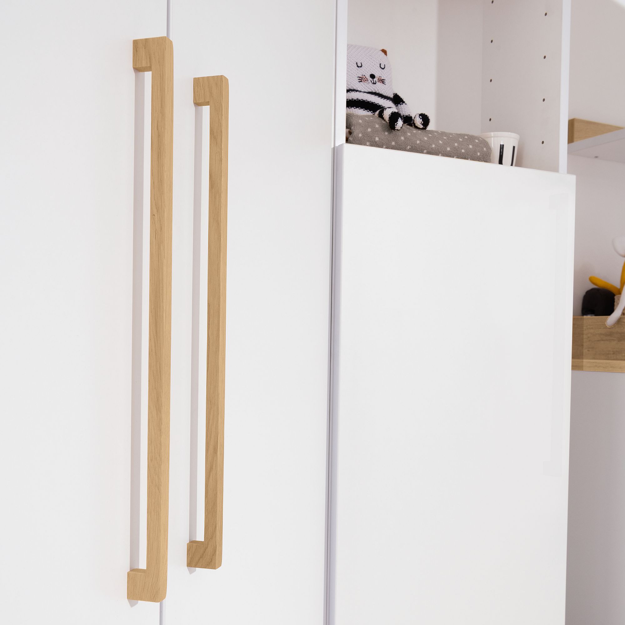 Weißer Schrank mit Holzgriffen und einem kleinen Stofftier auf dem Regal darüber.