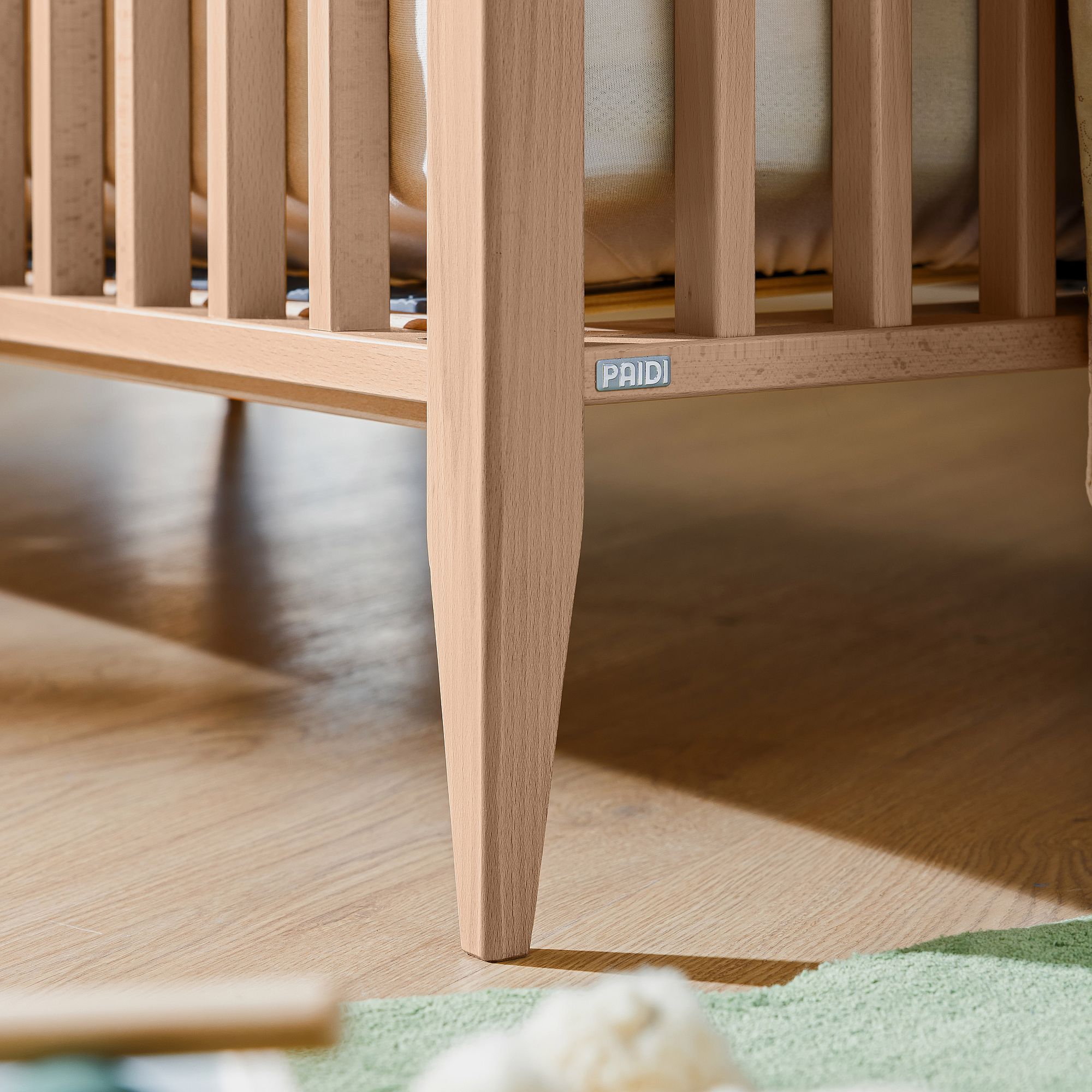 Nahaufnahme eines hölzernen Krippenbeins auf einem Holzboden mit einem grünen Teppich in der Nähe.