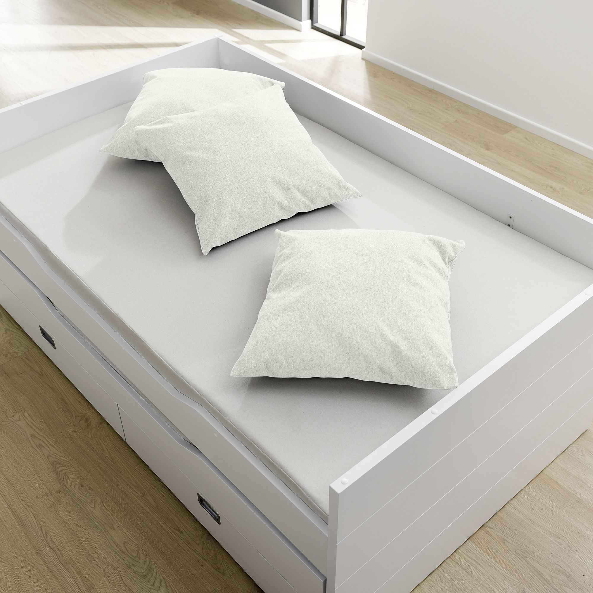 White bed with two white pillows in a bright room with wooden floor.