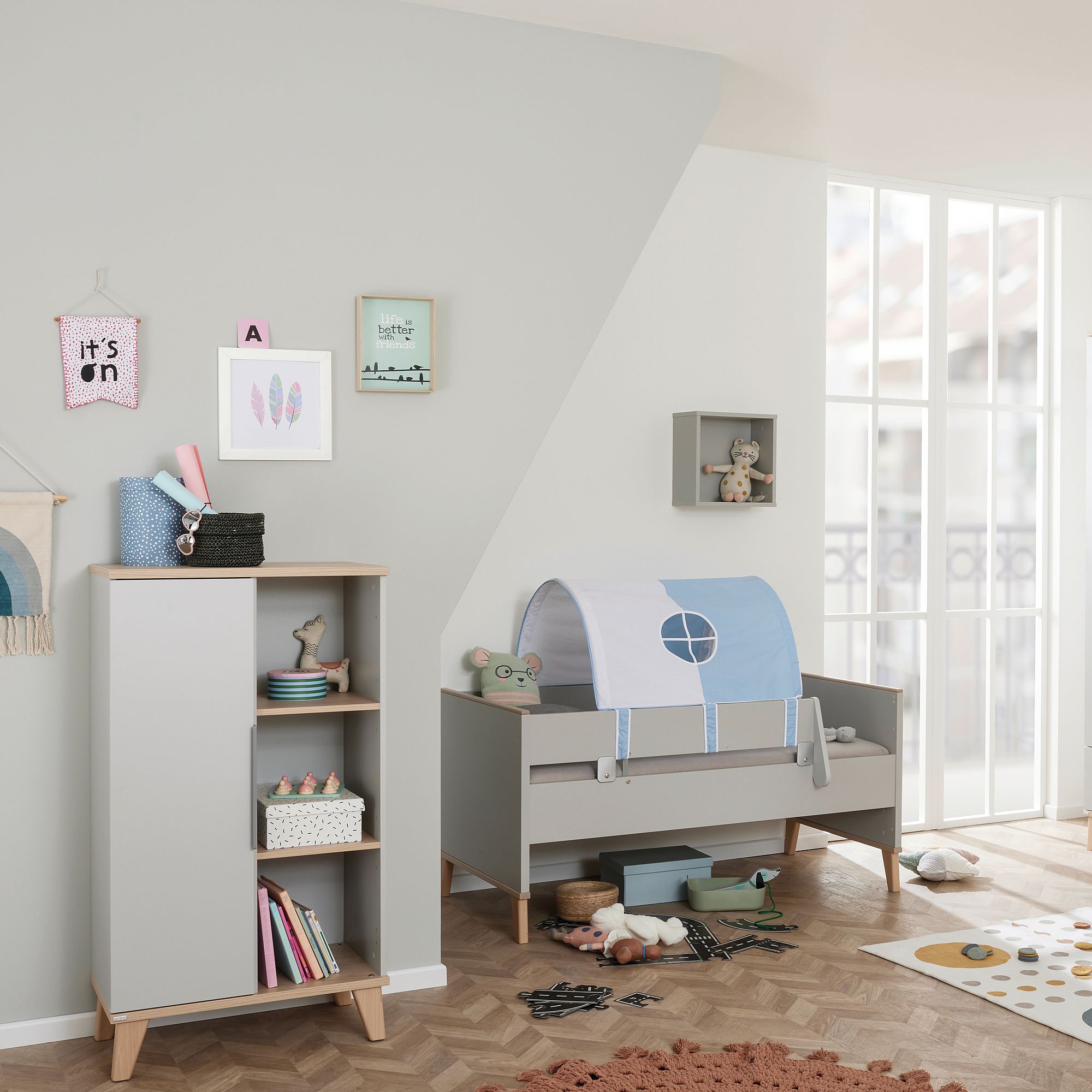 Modern nursery with a gray crib, bookshelf, toys, and wall art in soft colors.