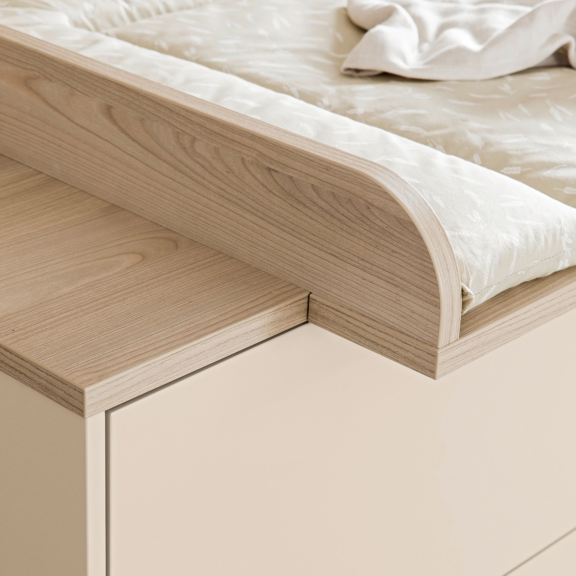 Nahaufnahme eines Wickeltisches aus hellem Holz mit einer gepolsterten Matte und einer Decke.