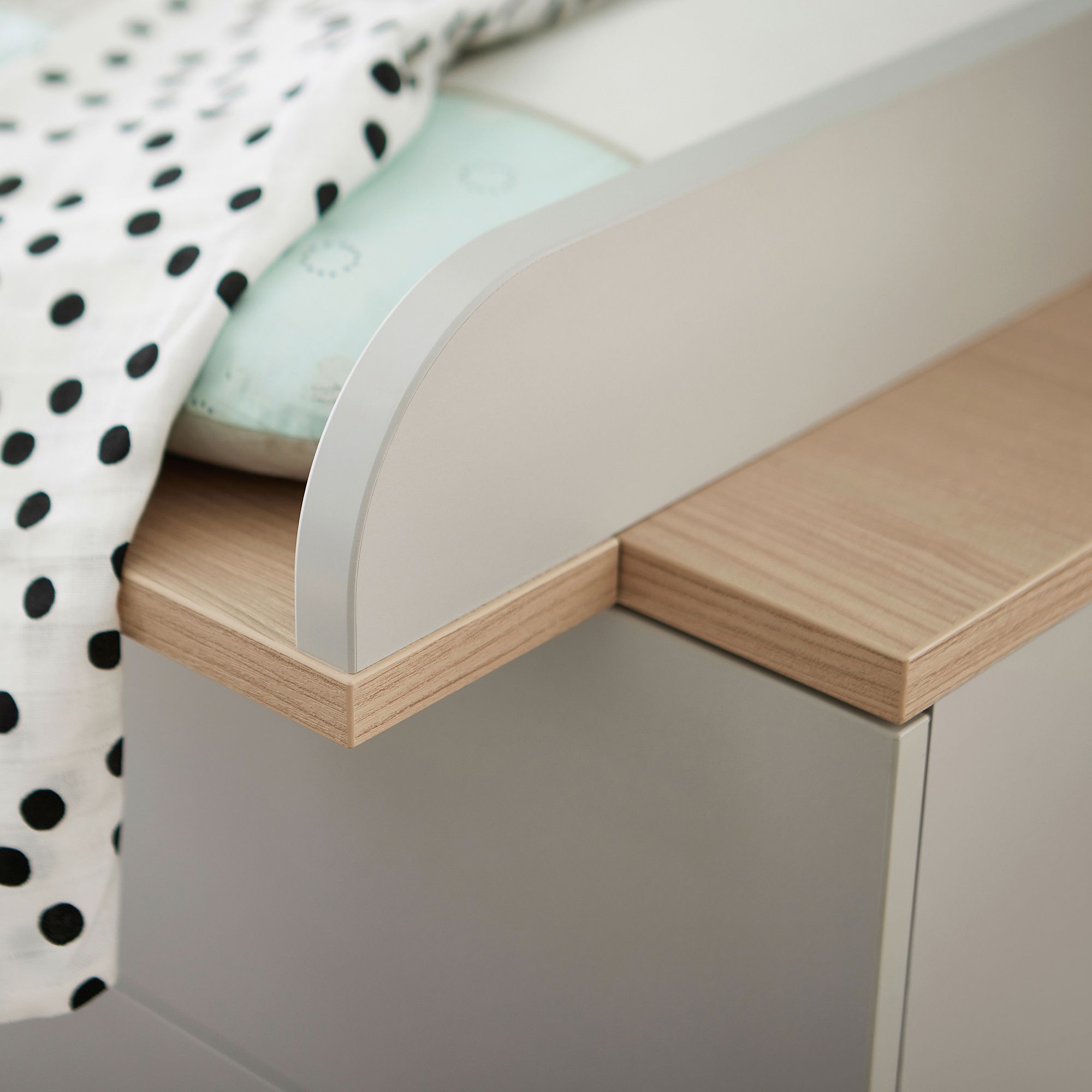 Nahaufnahme einer Krippenecke mit einer gepunkteten Decke und hellen Holzdetails.