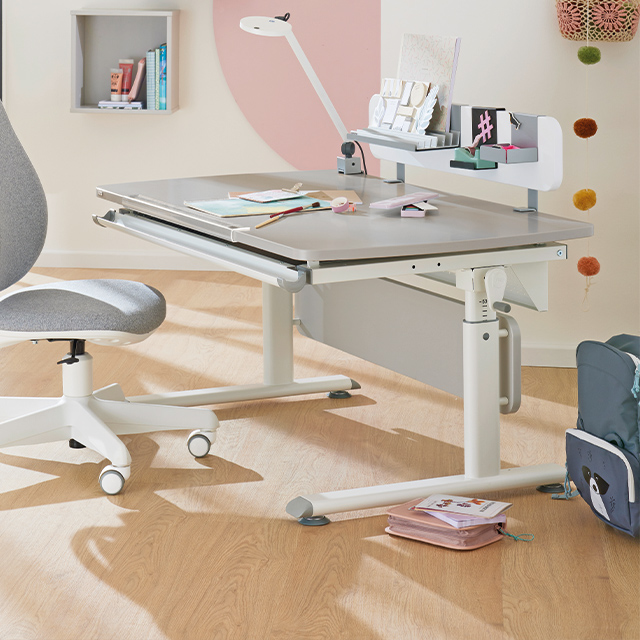 Modern study desk with books, stationery, and a gray chair on a wooden floor.