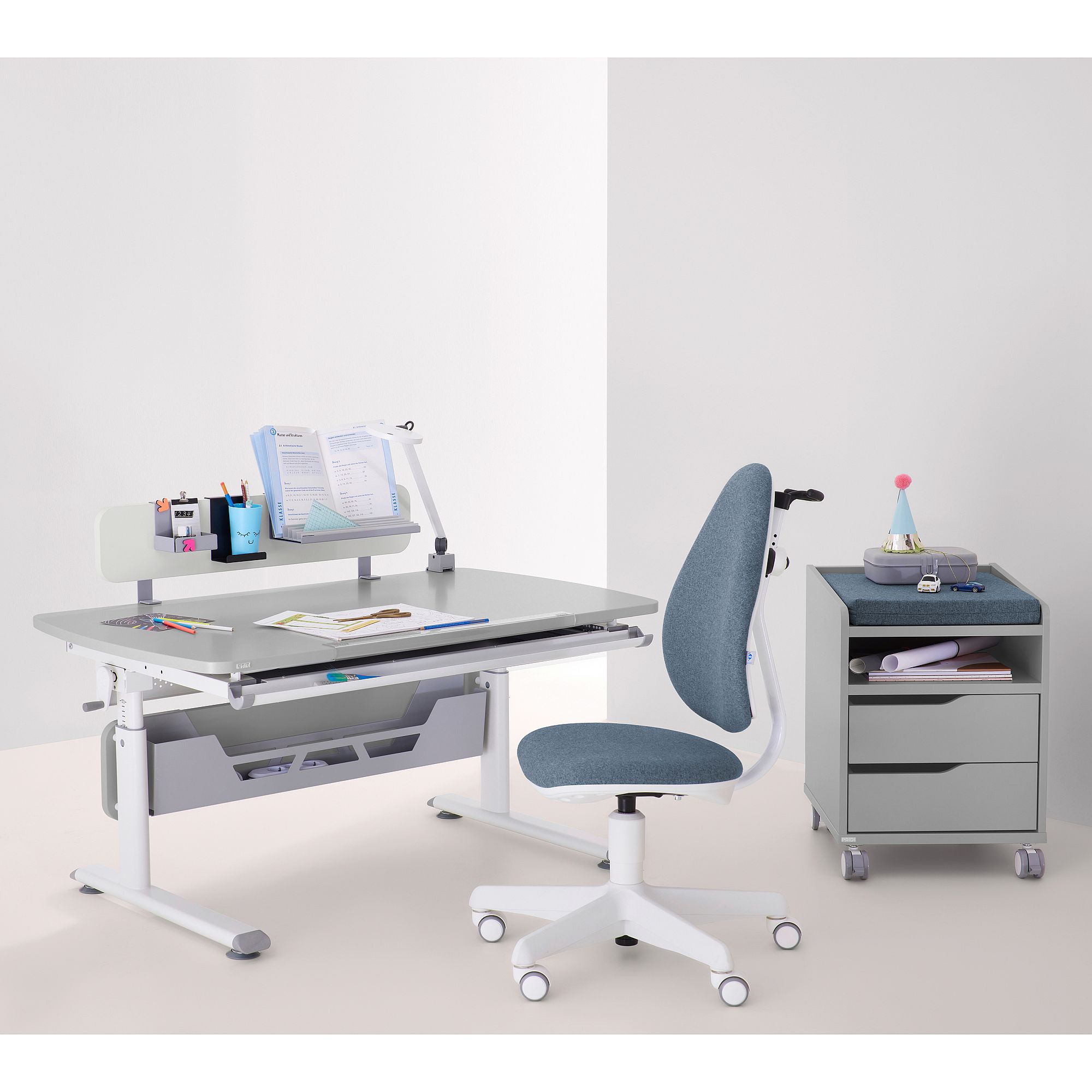 Schülerschreibtisch Diego Curved 120 x 70 cm in Kieselgrau Moderner Schreibtisch mit Büchern, Material, einem Rollstuhl und einem kleinen Schubladenblock.