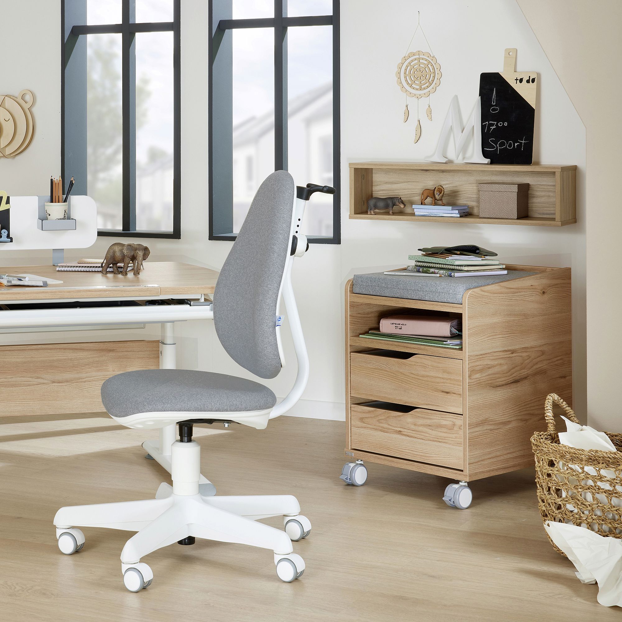 Modern home office with a gray chair, wooden desk, drawers, and decor items.