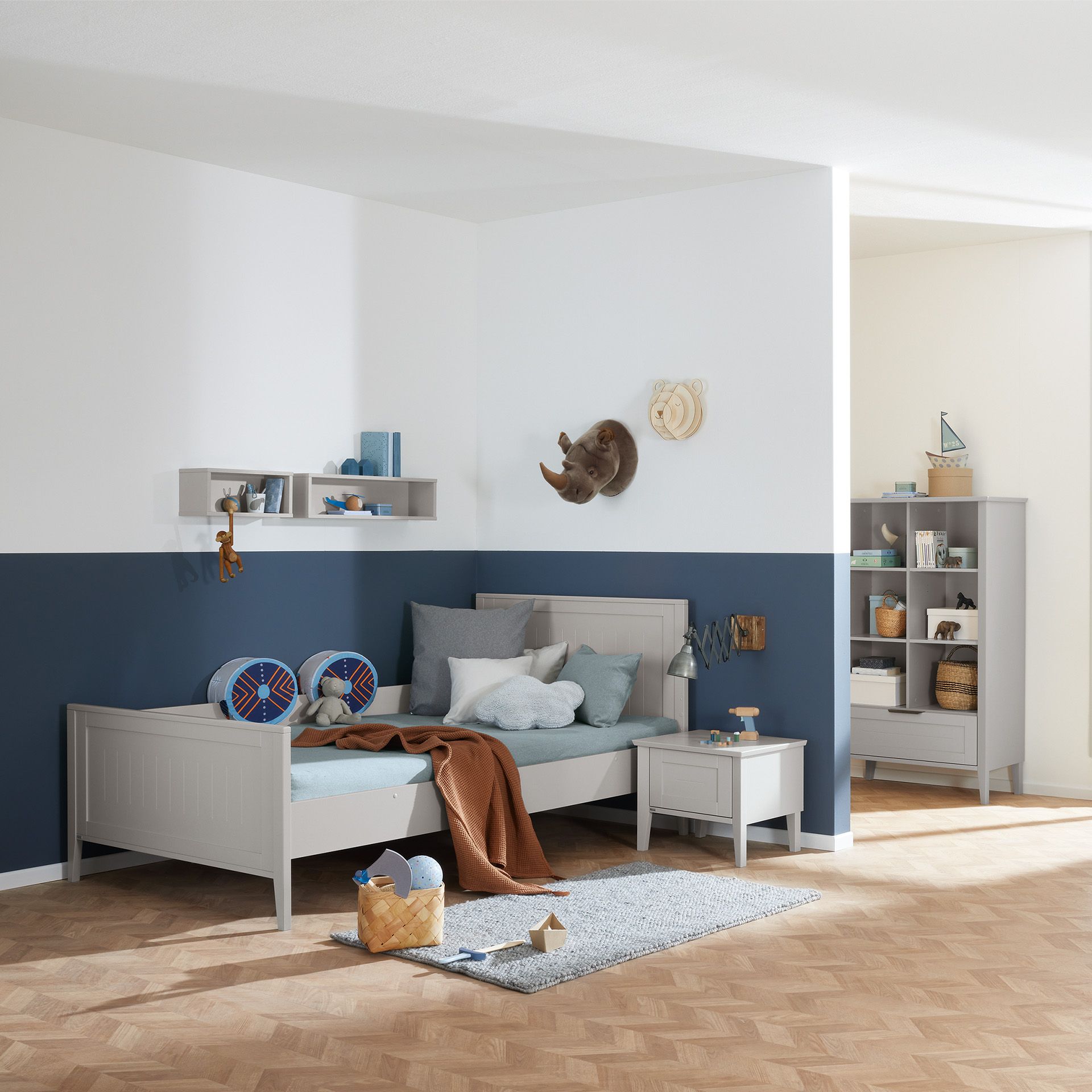 Kinderzimmer mit blauer Wand, Bett, Regalen und Wanddekoration mit Tiermotiven.