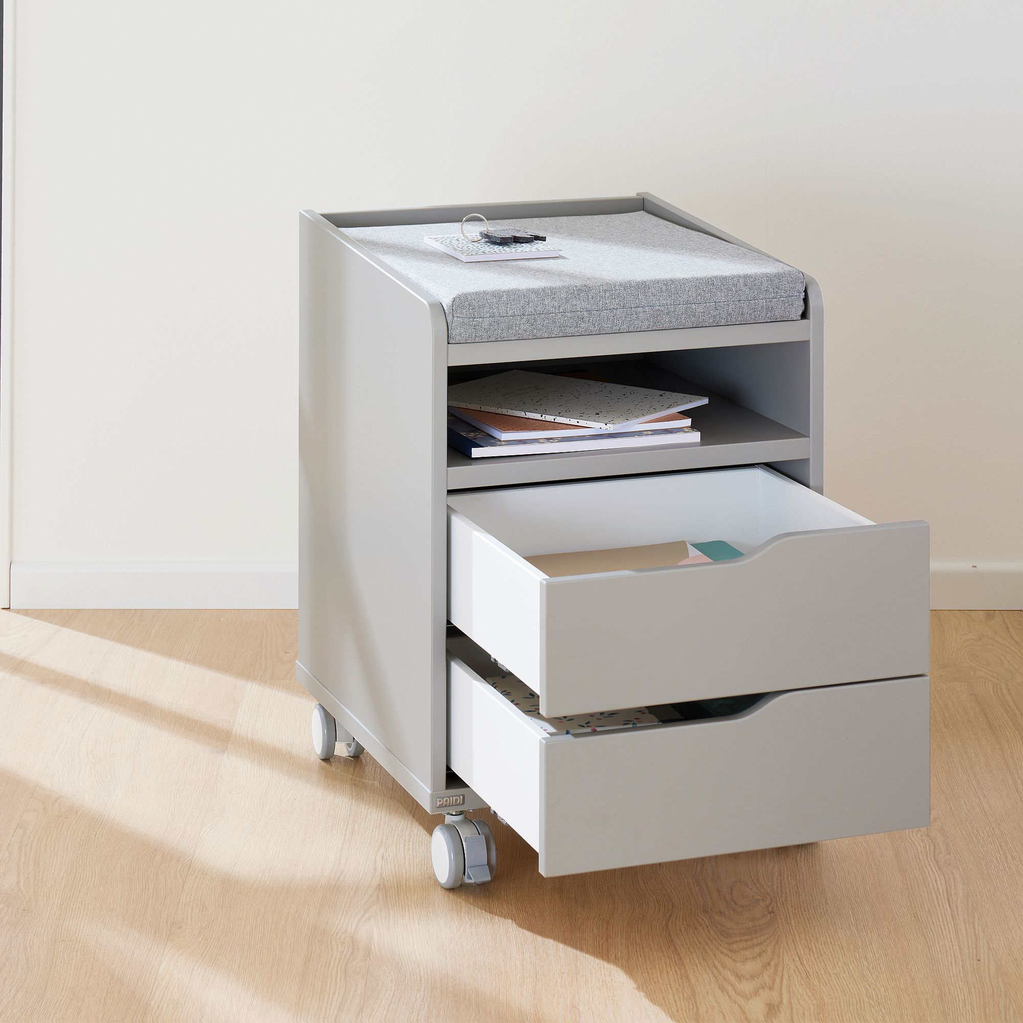 Rollcontainer  mit 2 Schubladen in Kieselgrau Ein grauer rollender Aufbewahrungswagen mit zwei offenen Schubladen und einer gepolsterten Platte.