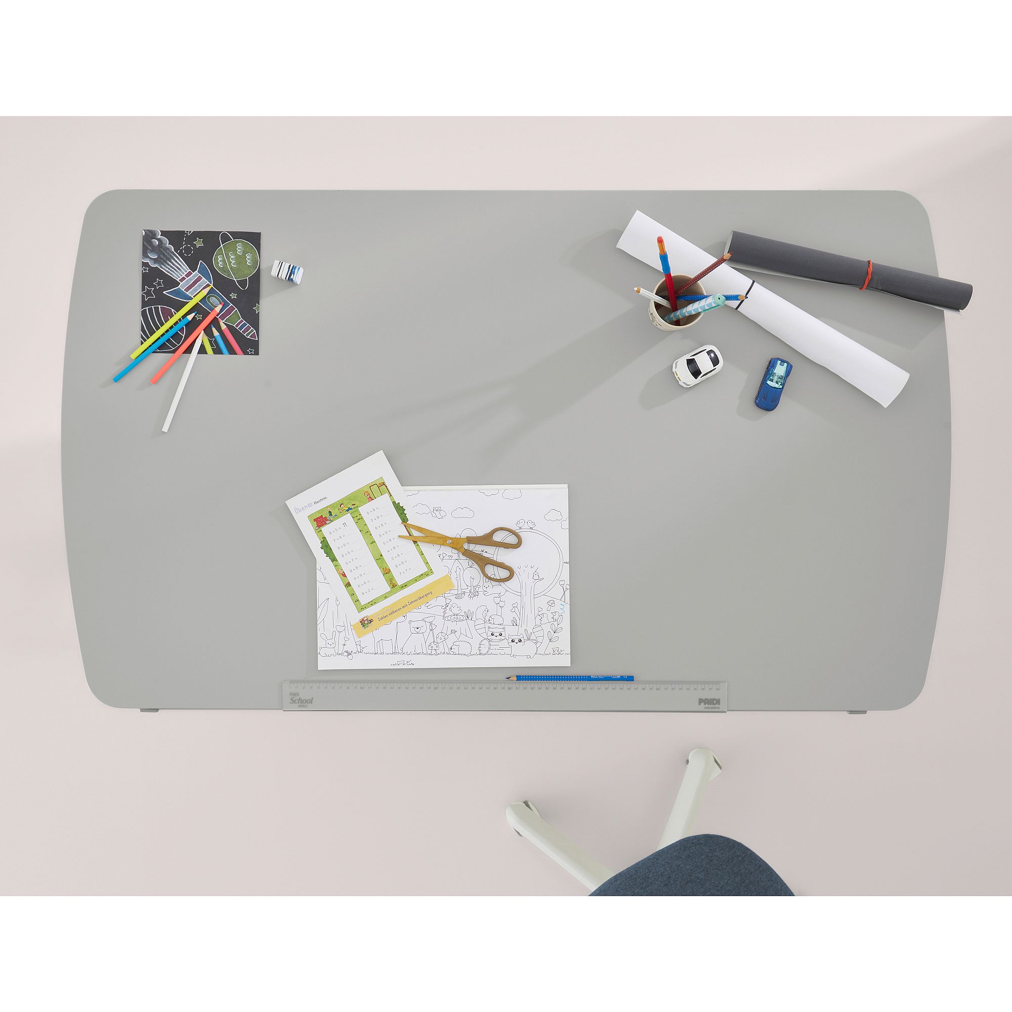 Schülerschreibtisch Diego Curved 120 x 70 cm in Kieselgrau Grauer Schreibtisch mit Papieren, Buntstiften, Scheren und Schreibwaren darauf.