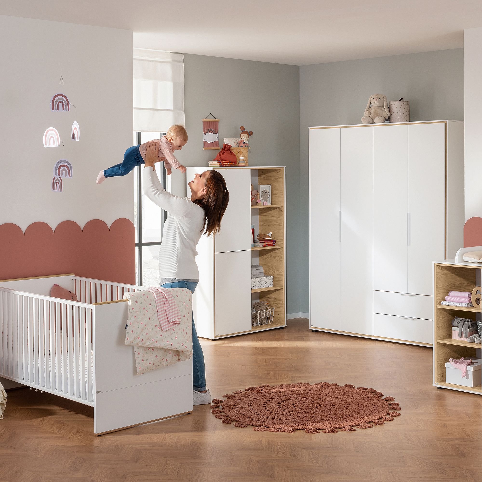 Eine Mutter hält ihr Baby in einem gemütlichen, modernen Kinderzimmer mit pastellfarbenen Dekorationen und Möbeln im Arm.