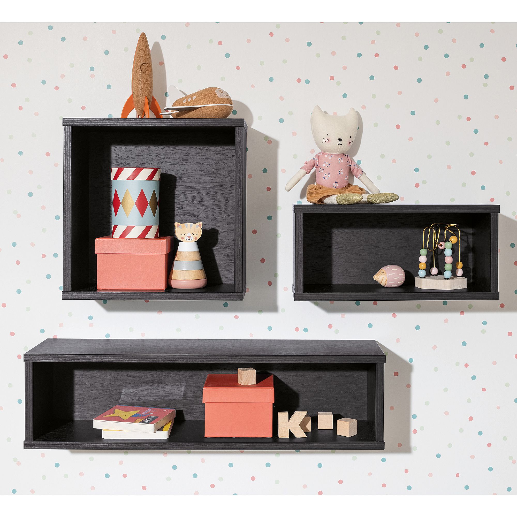 Drei schwarze Wandregale mit Spielzeug, Büchern und Kisten vor einer gepunkteten Wand.