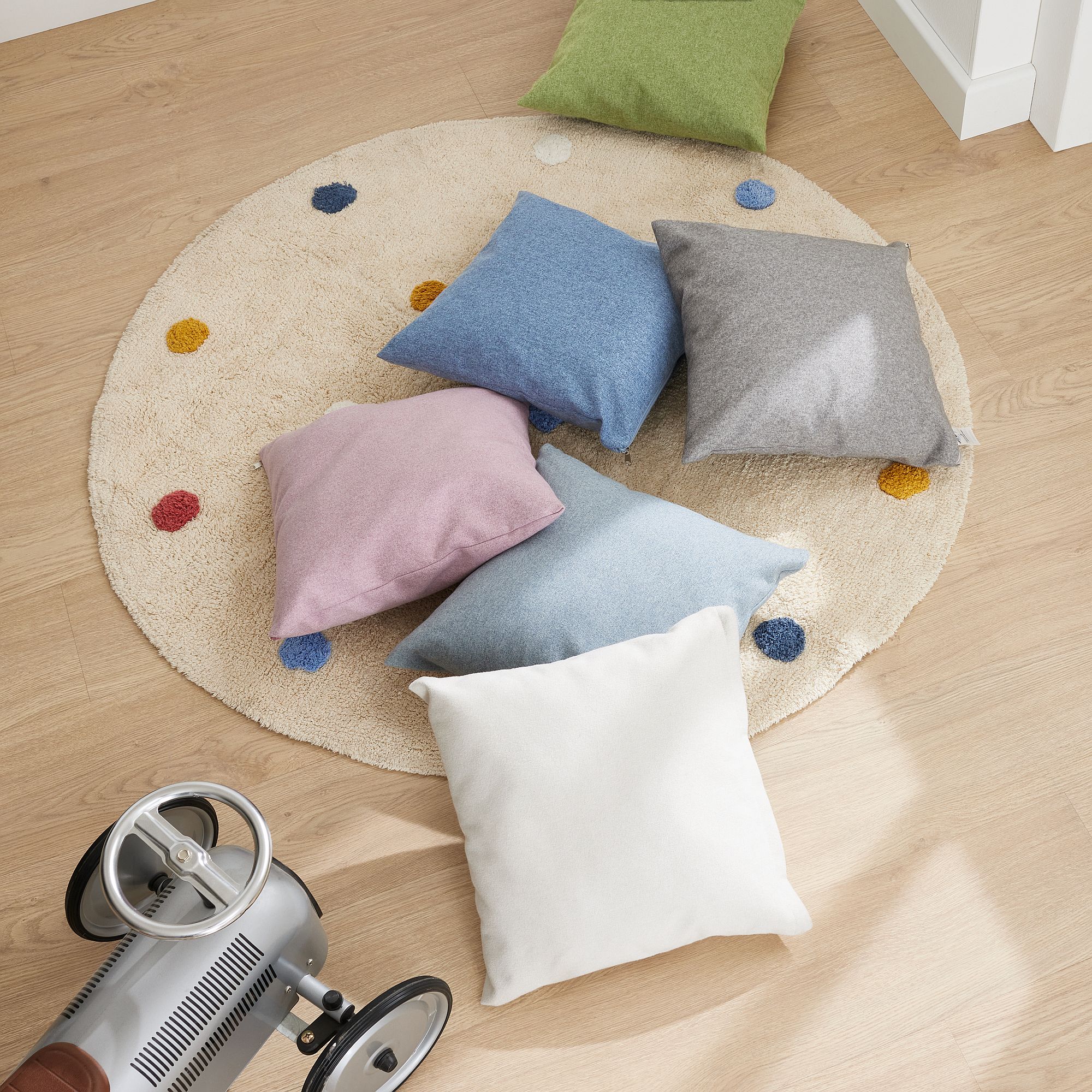 Partykissen  40 x 40 cm im Mikrofaserbezug Ivory Sechs bunte Kissen auf einem runden Teppich mit Punkten, neben einem silbernen Spielzeugauto auf Holzboden.