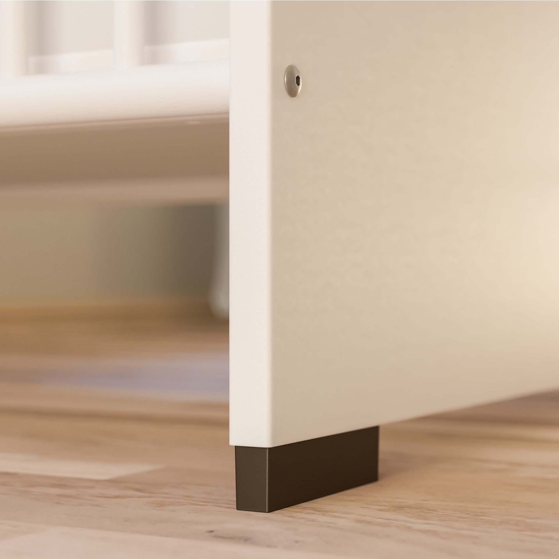 Close-up of a white crib leg with a dark base on a wooden floor.