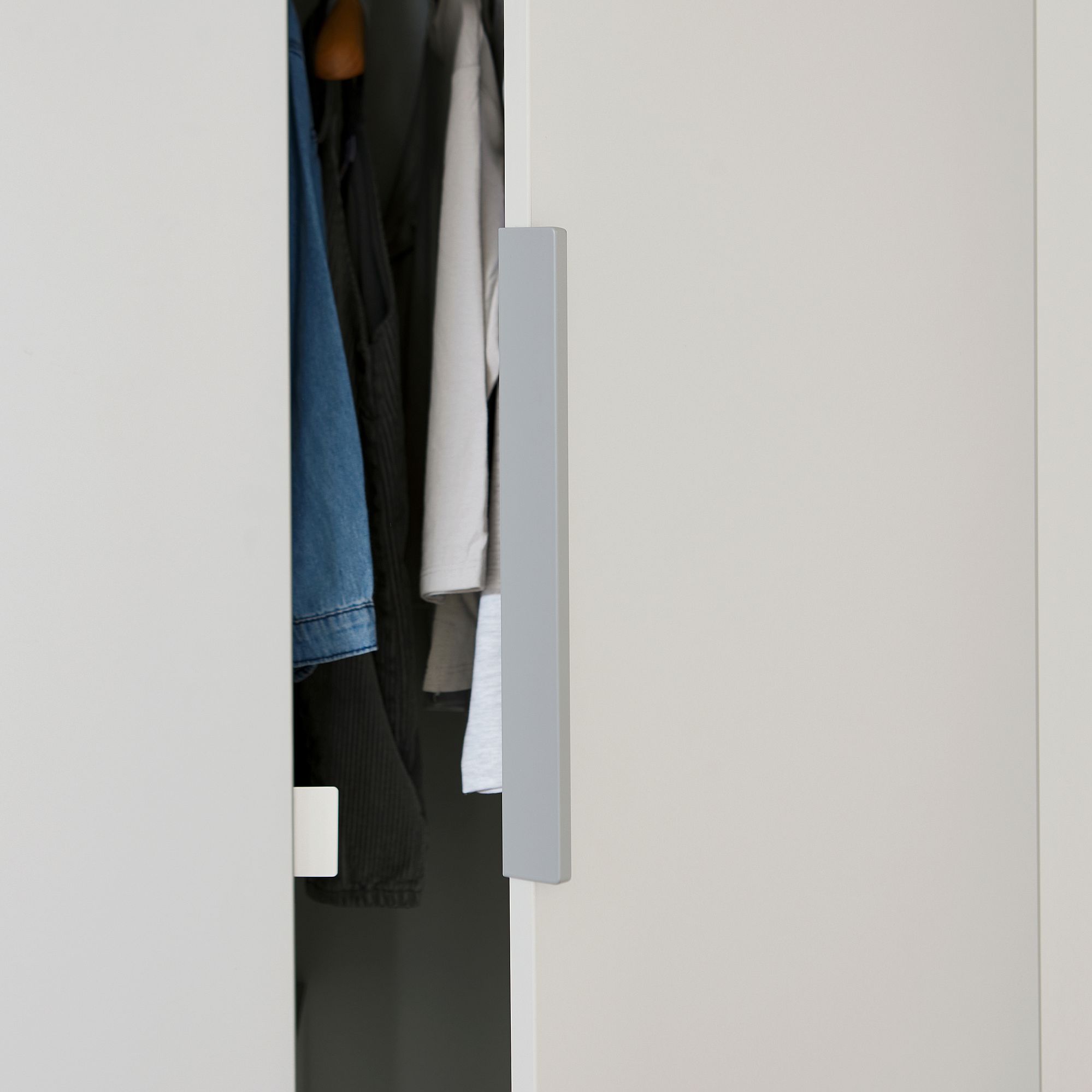 Drehtürenschrank Fiene mit 4 Türen und 1 Schublade Teilweise geöffnete weiße Schranktür, in der Kleidung hängt.