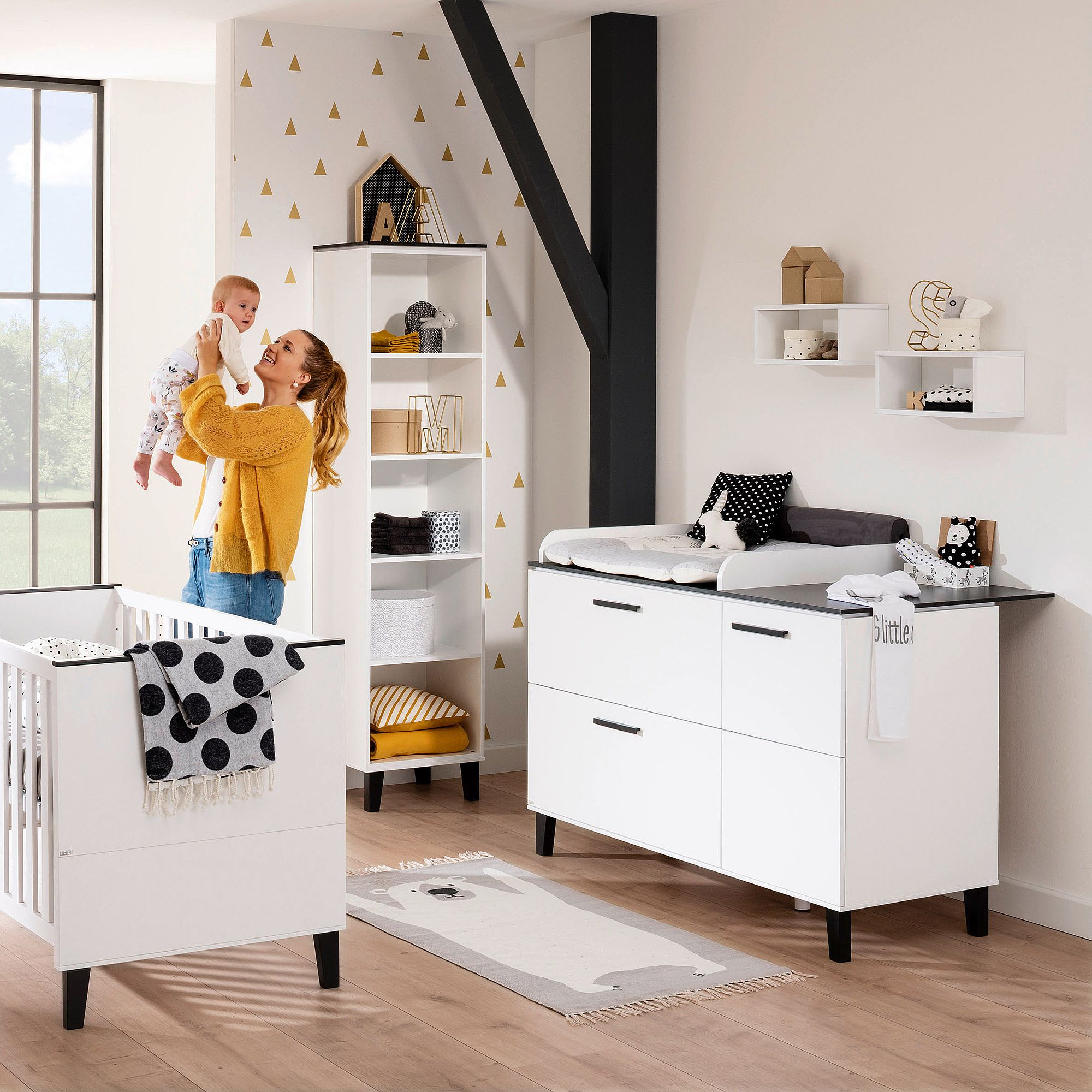 Eine Frau, die ein Baby im Arm hält, in einem modernen, weiß-gelben Kinderzimmer.
