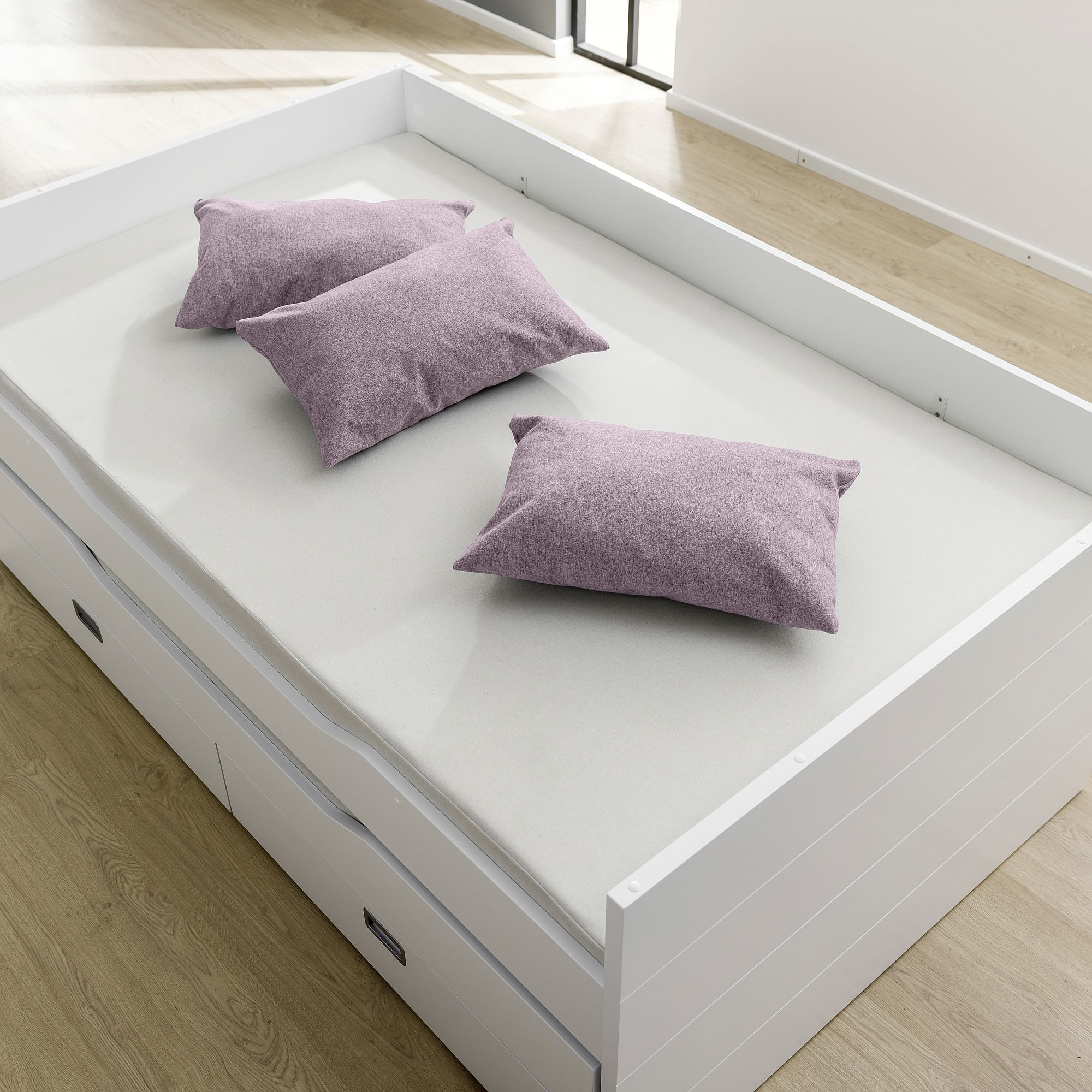 White bed with three purple pillows on a light mattress in a bright room.