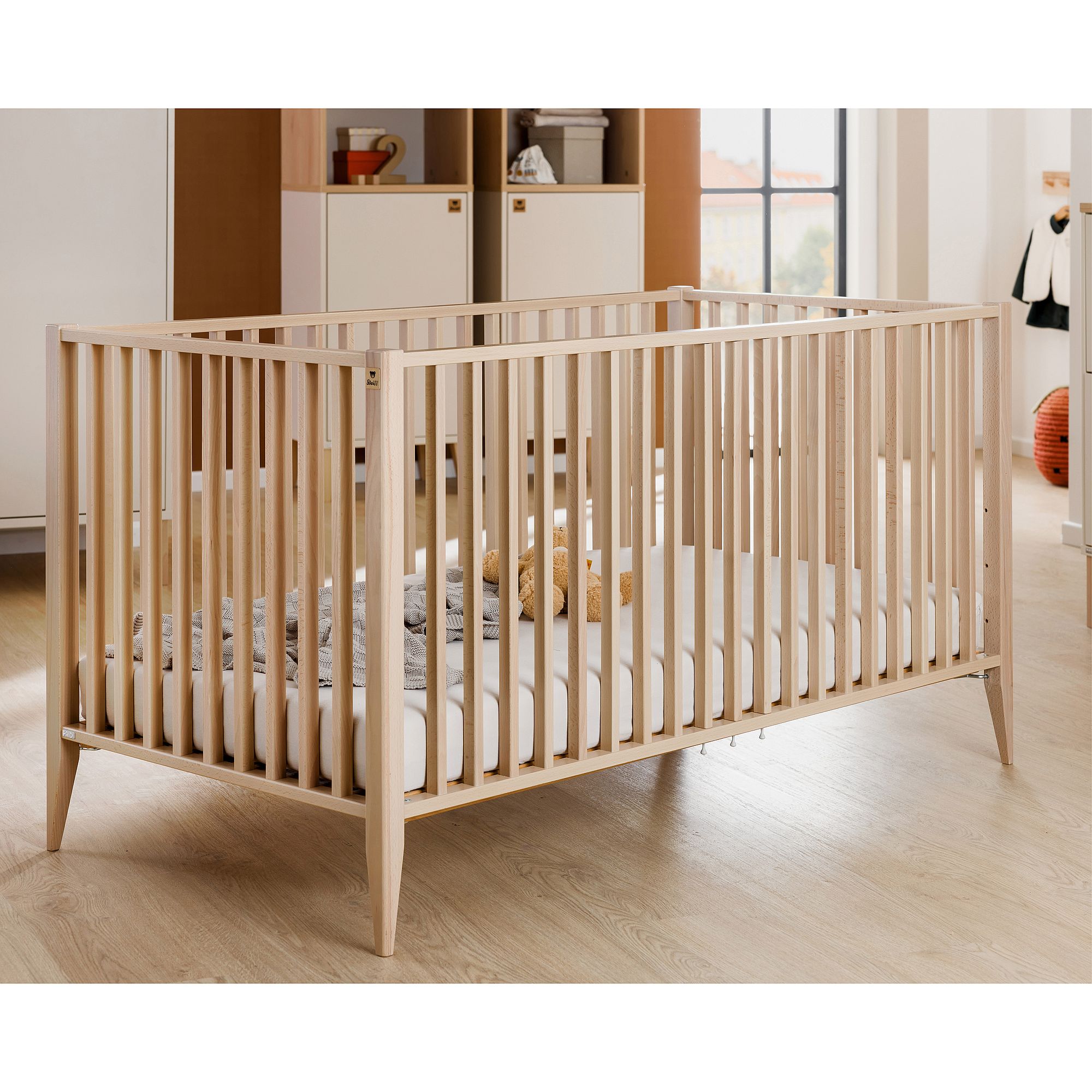 Babybett aus hellem Holz mit Bettzeug und Spielzeug in einem modernen Kinderzimmer.