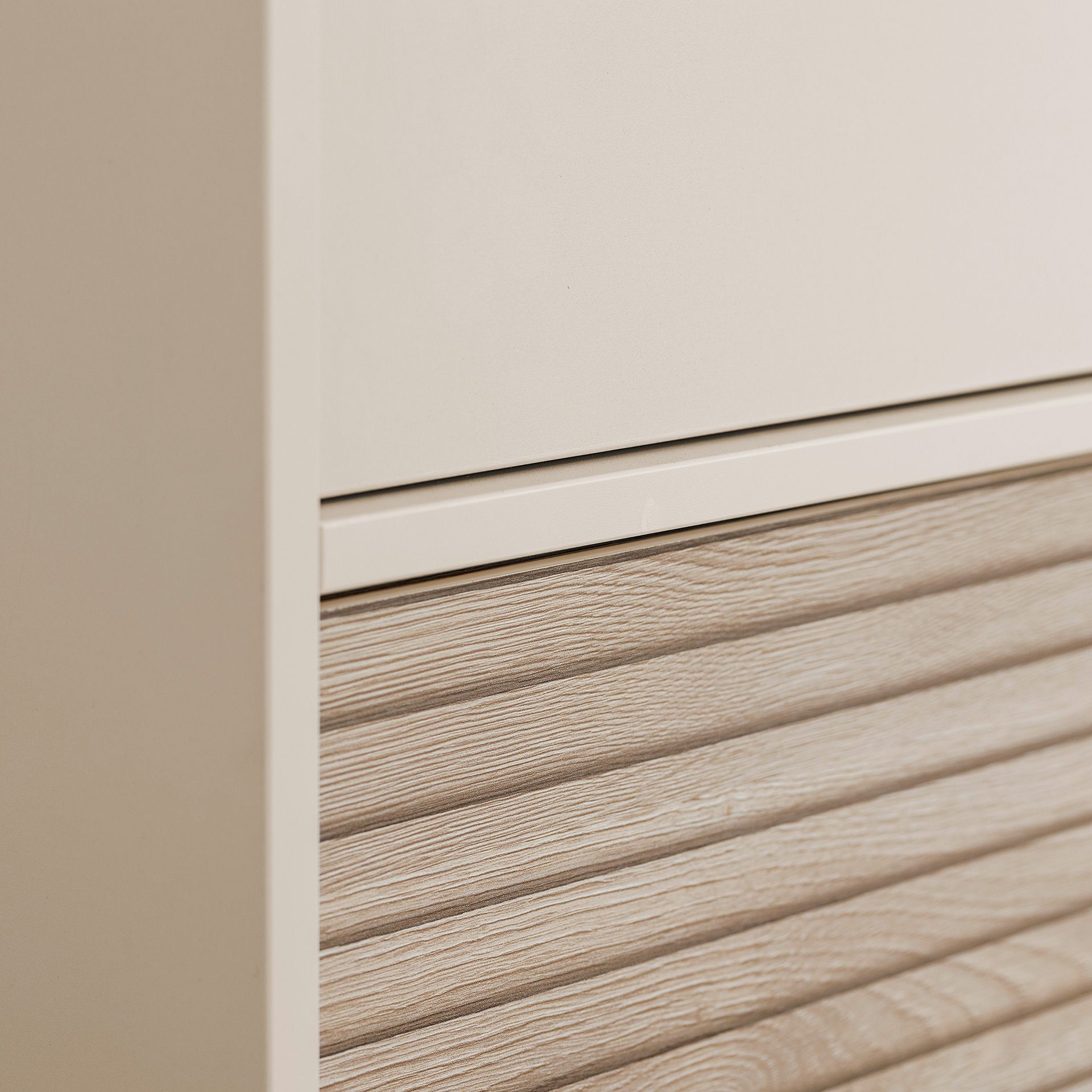 Nahaufnahme eines Schranks mit einer glatten, beigen Schublade über einer Schublade aus strukturiertem Holz.